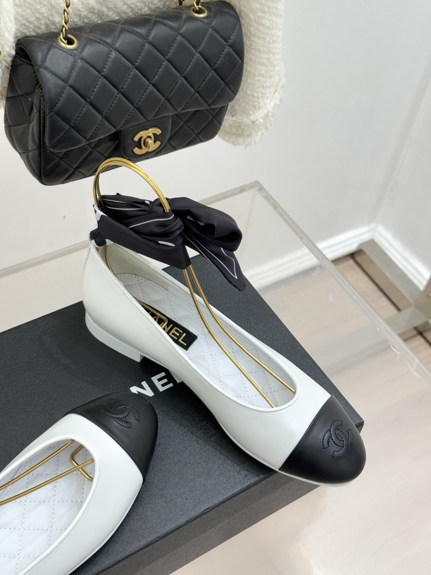Luxury white Chanel ballerina flats with black toe caps and black silk ribbon bows displayed on a black brand box. - Hình 5