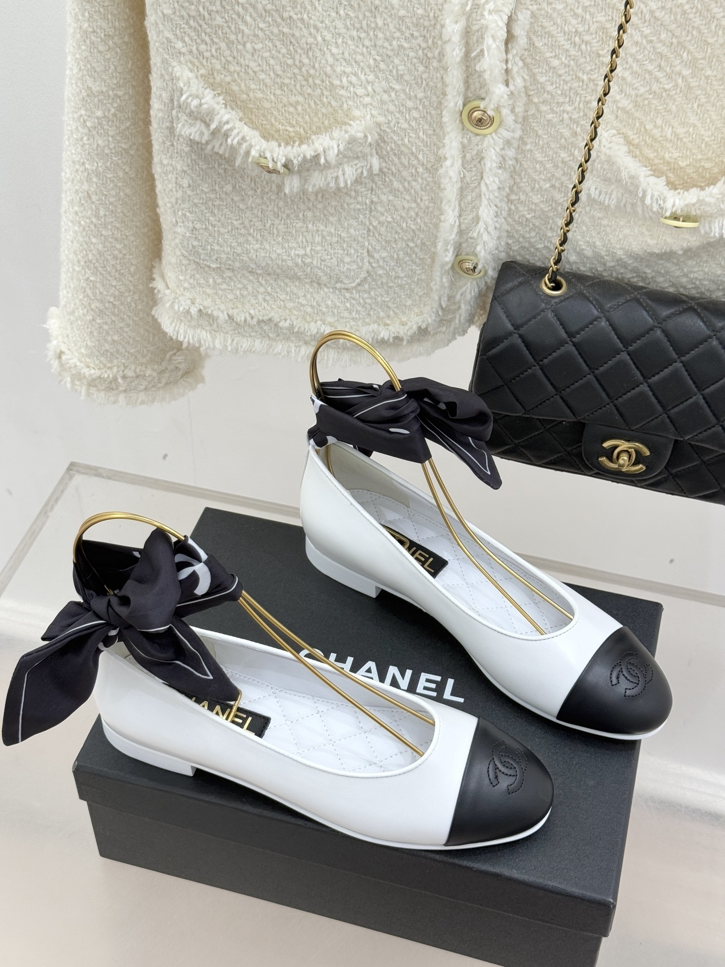 Luxury white Chanel ballerina flats with black toe caps and black silk ribbon bows displayed on a black brand box. - Hình 3