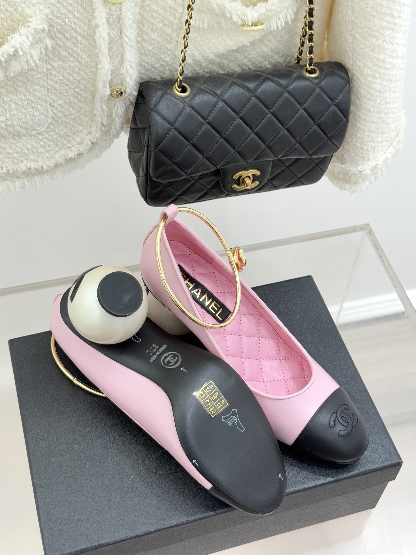 Chanel pink and black two-tone leather pumps with a large white pearl-shaped heel and gold-tone ankle ring displayed on a black box. - Hình 9