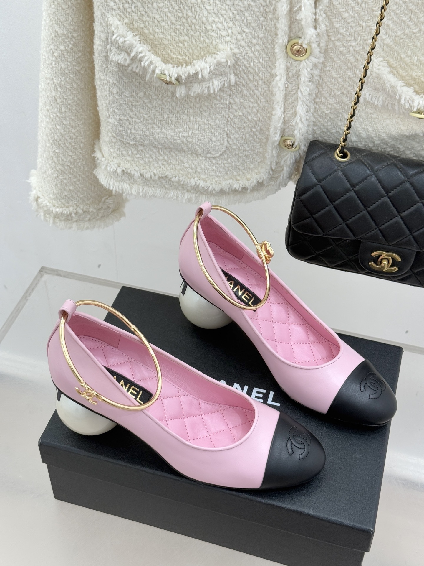 Chanel pink and black two-tone leather pumps with a large white pearl-shaped heel and gold-tone ankle ring displayed on a black box. - Hình 3