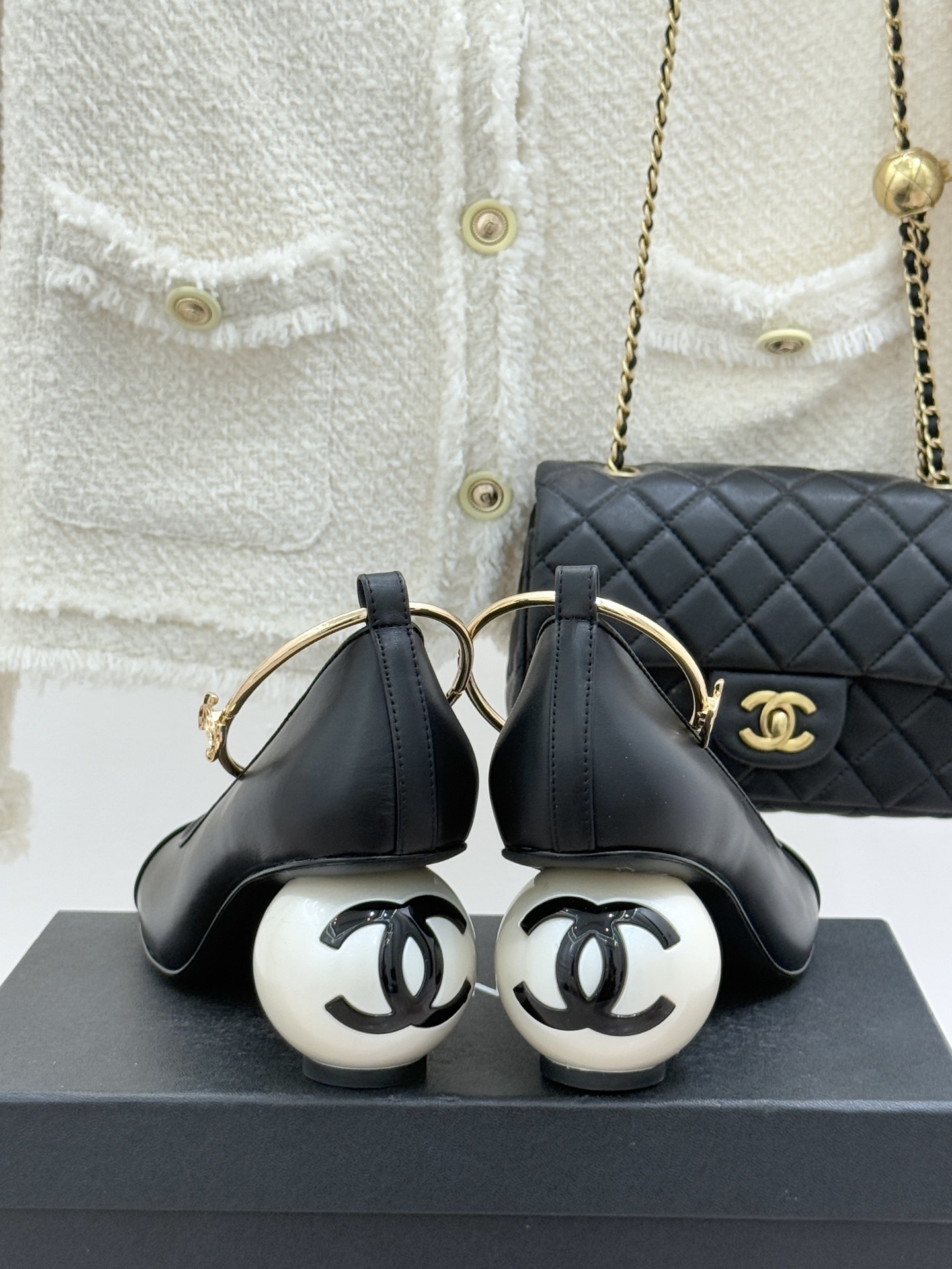A pair of Chanel black leather pumps featuring unique white spherical pearl heels and gold-tone ankle straps with the CC logo. - Hình 6