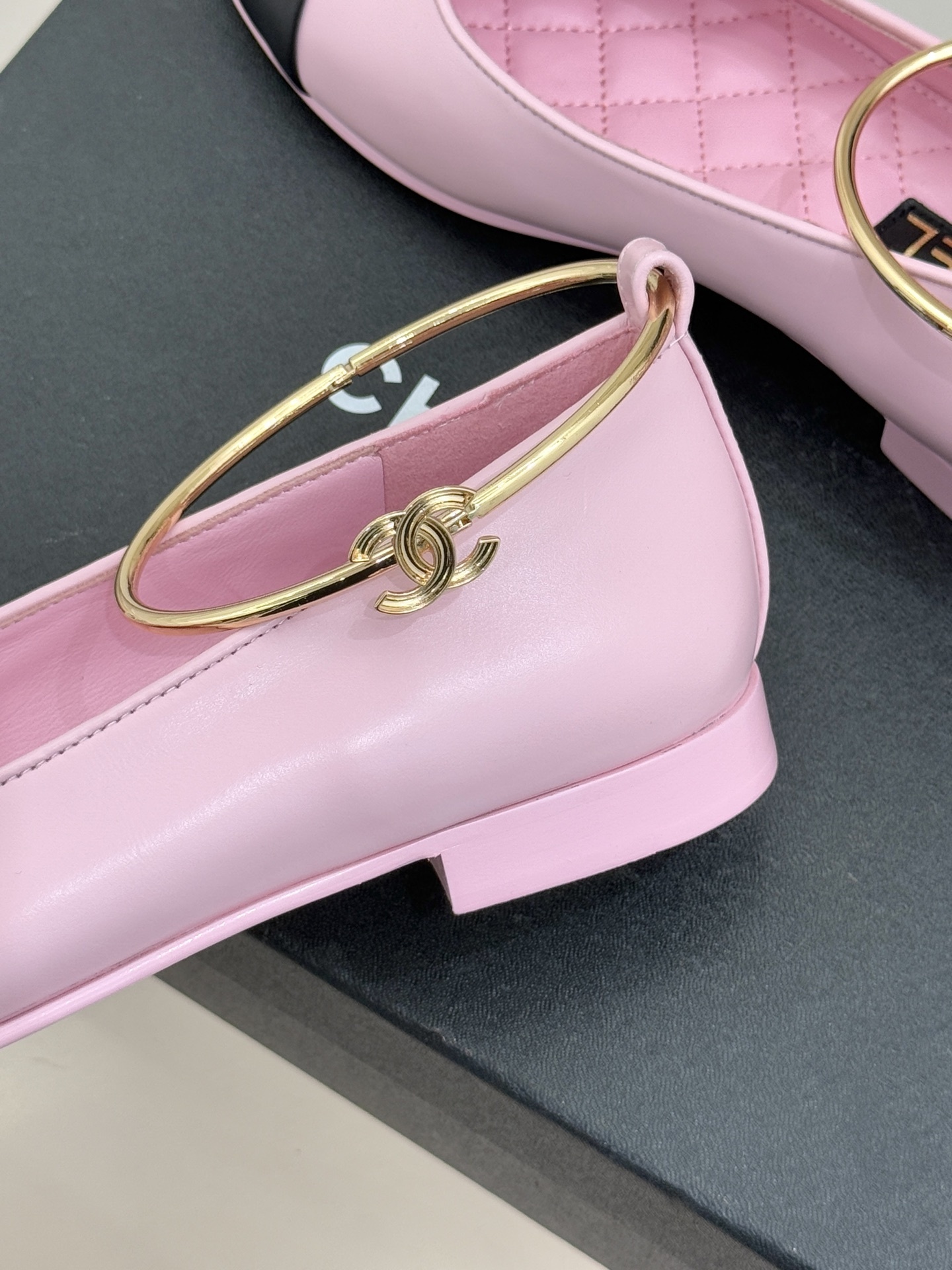 A pair of Chanel pink leather ballerina flats with black cap-toes and gold-tone metal ankle rings resting on a black box. - Hình 6