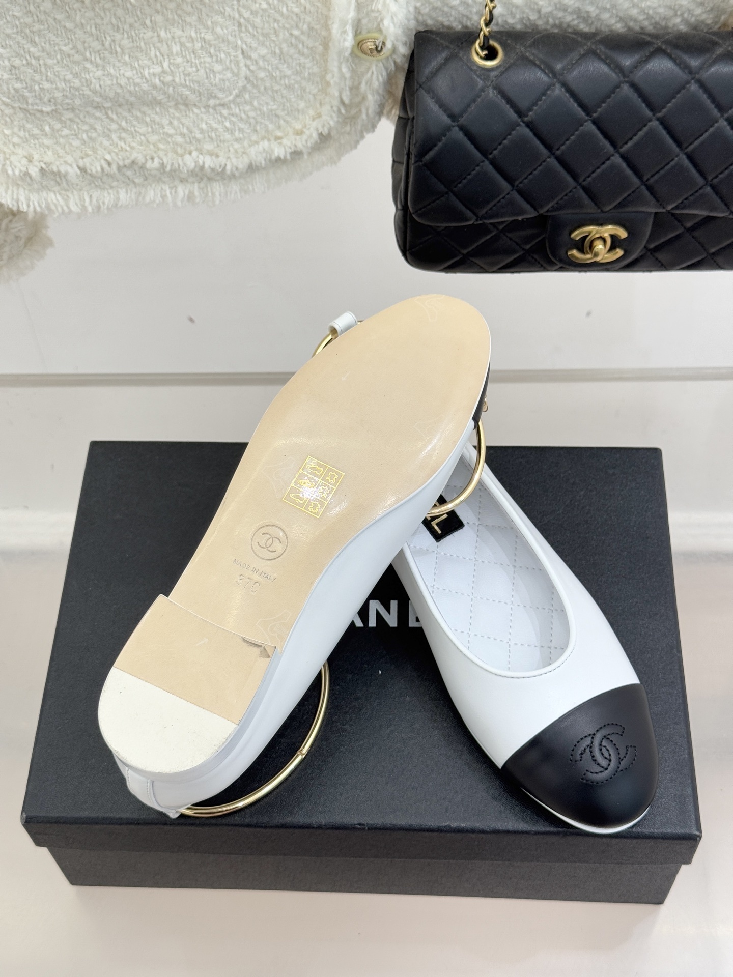 Pair of Chanel white leather ballet flats with black cap-toes and gold CC ankle rings displayed on a black Chanel box. - Hình 9
