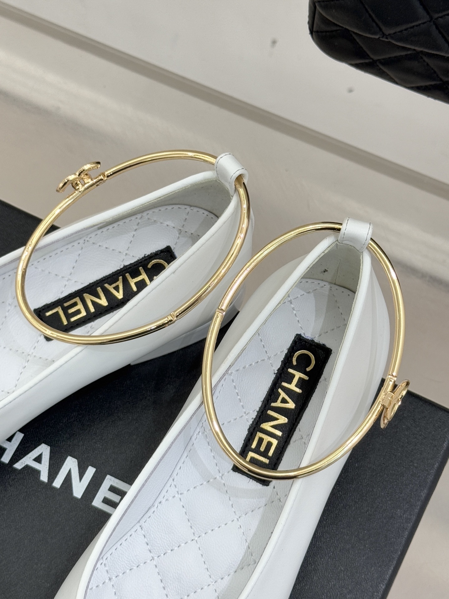 Pair of Chanel white leather ballet flats with black cap-toes and gold CC ankle rings displayed on a black Chanel box. - Hình 8