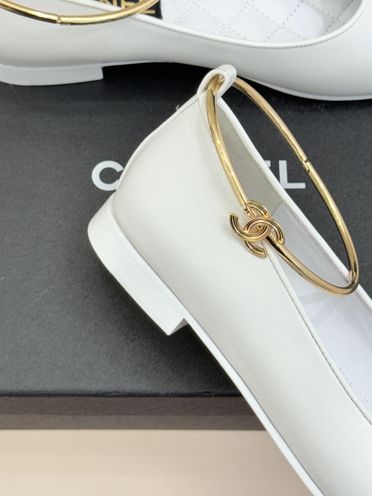 Pair of Chanel white leather ballet flats with black cap-toes and gold CC ankle rings displayed on a black Chanel box. - Hình 5