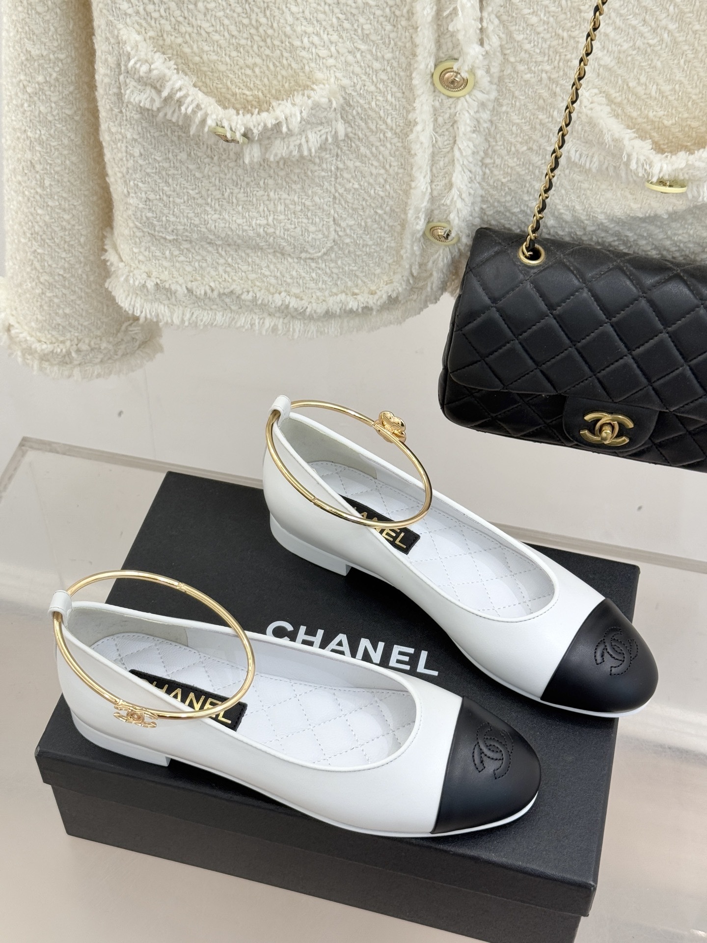 Pair of Chanel white leather ballet flats with black cap-toes and gold CC ankle rings displayed on a black Chanel box. - Hình 3