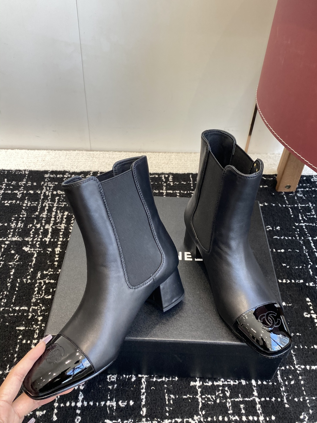 Pair of black Chanel leather ankle boots with patent leather cap-toe and CC logo on a black box. - Hình 8