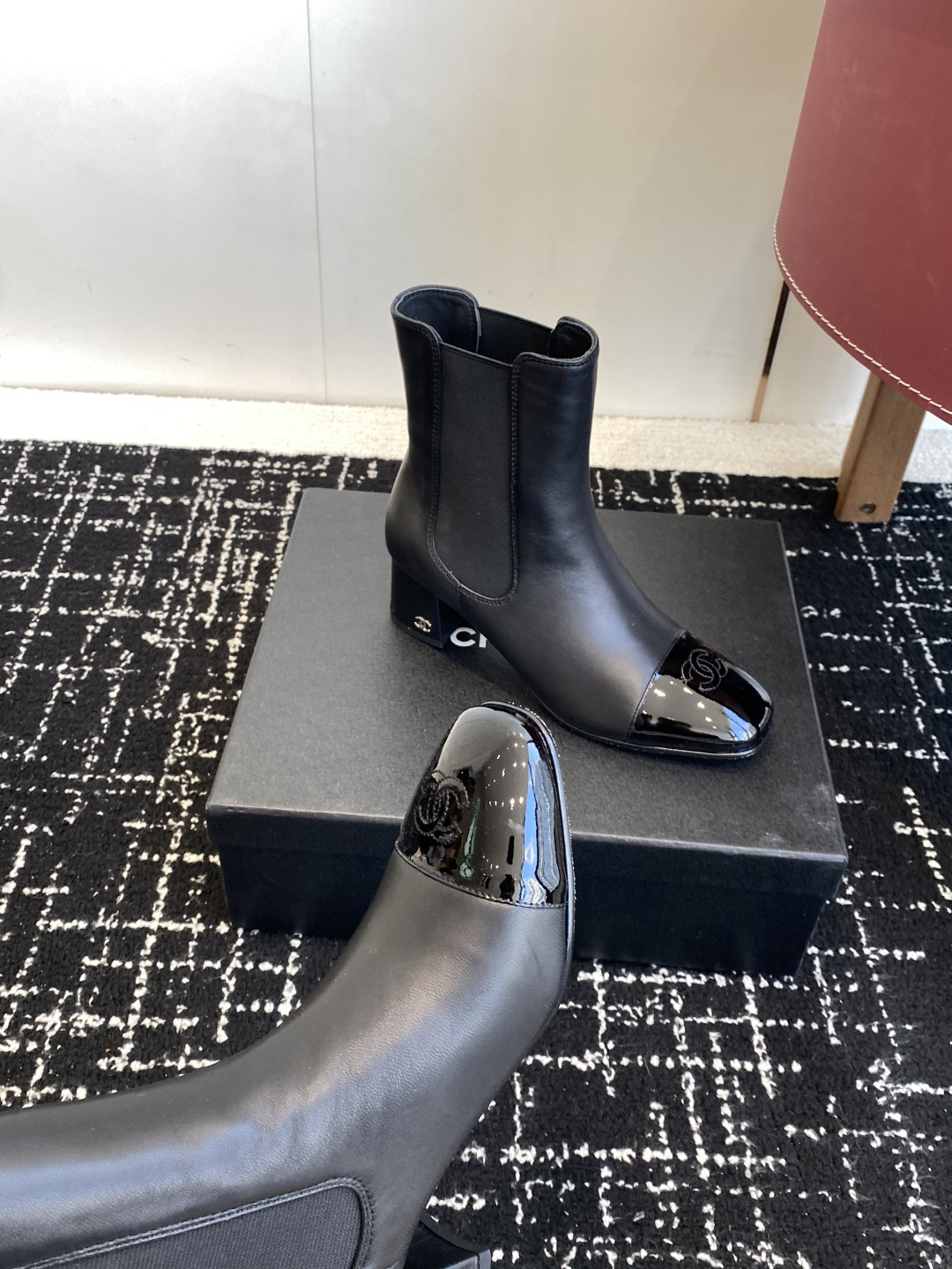 Pair of black Chanel leather ankle boots with patent leather cap-toe and CC logo on a black box. - Hình 7