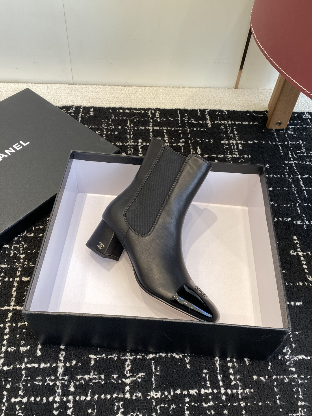 Pair of black Chanel leather ankle boots with patent leather cap-toe and CC logo on a black box. - Hình 6