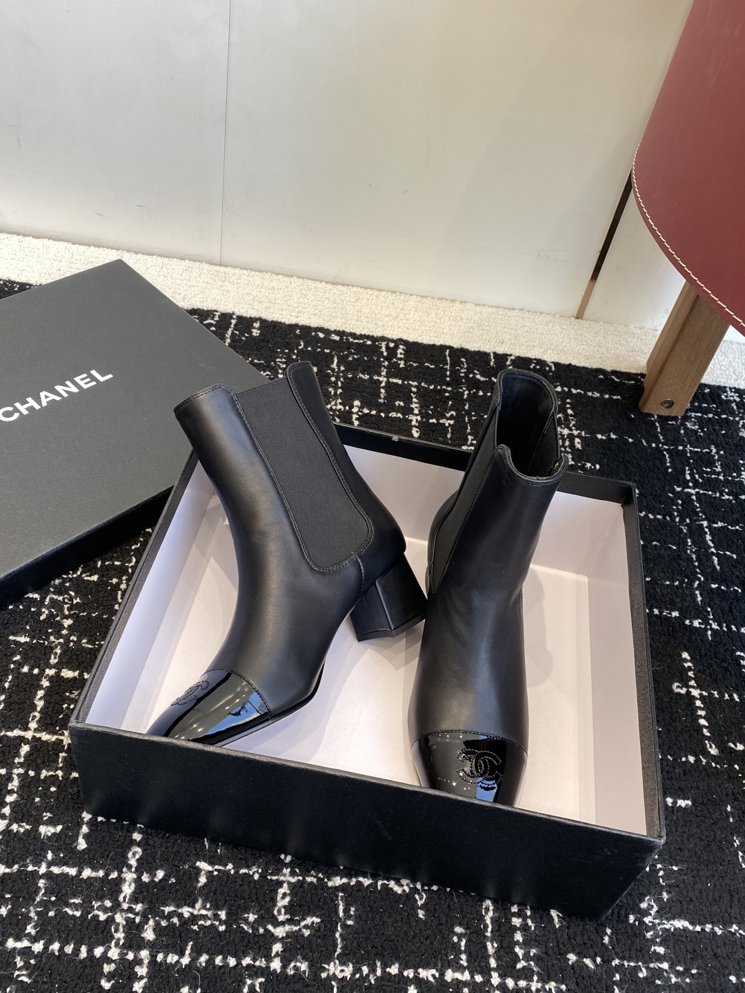 Pair of black Chanel leather ankle boots with patent leather cap-toe and CC logo on a black box. - Hình 5