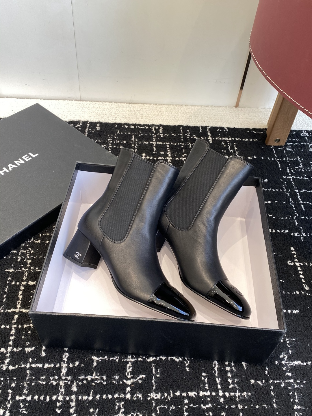Pair of black Chanel leather ankle boots with patent leather cap-toe and CC logo on a black box. - Hình 4