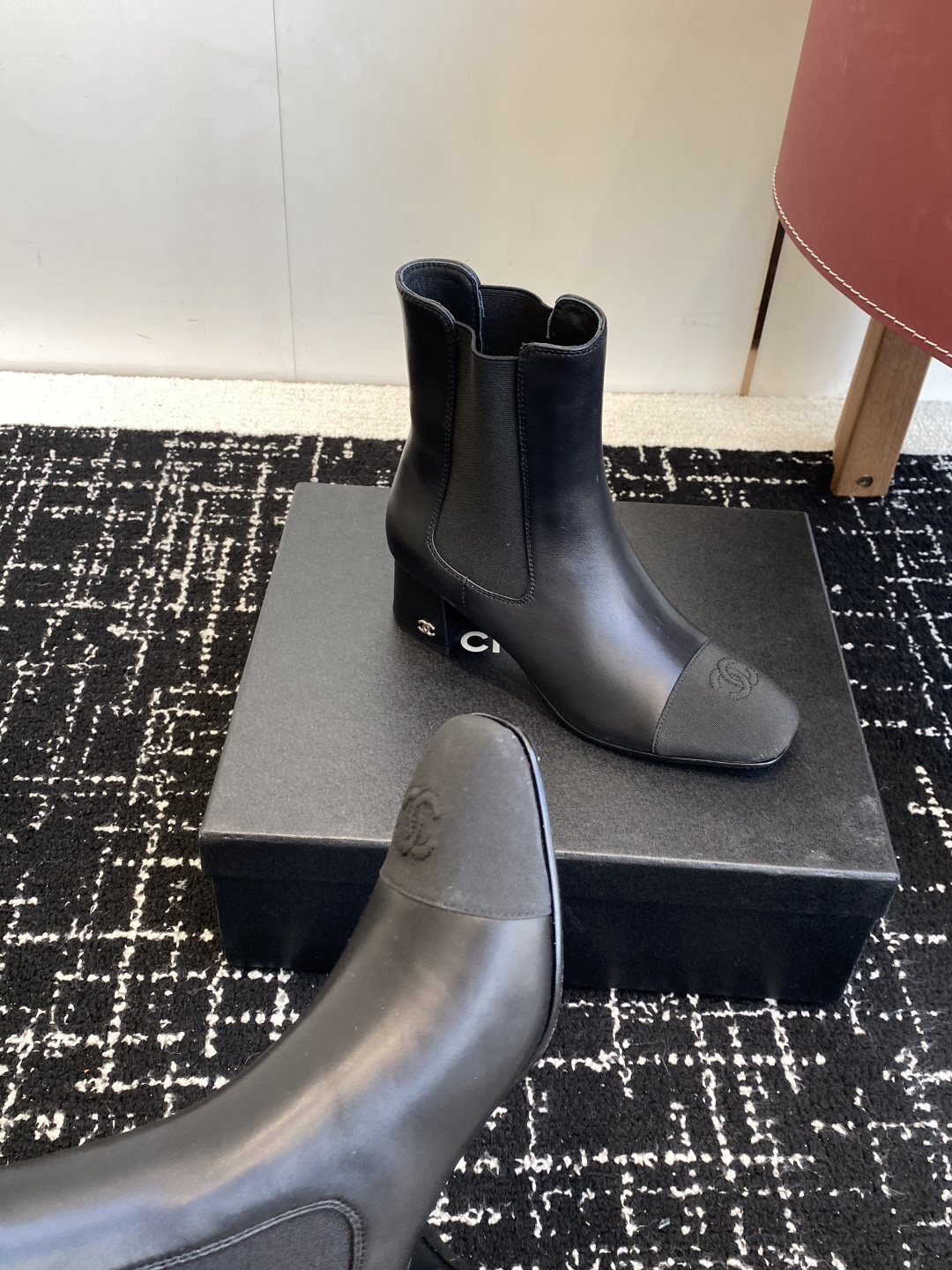 Chanel black leather Chelsea boots with signature CC logo on the toe cap and heel, displayed on a black box. - Hình 7
