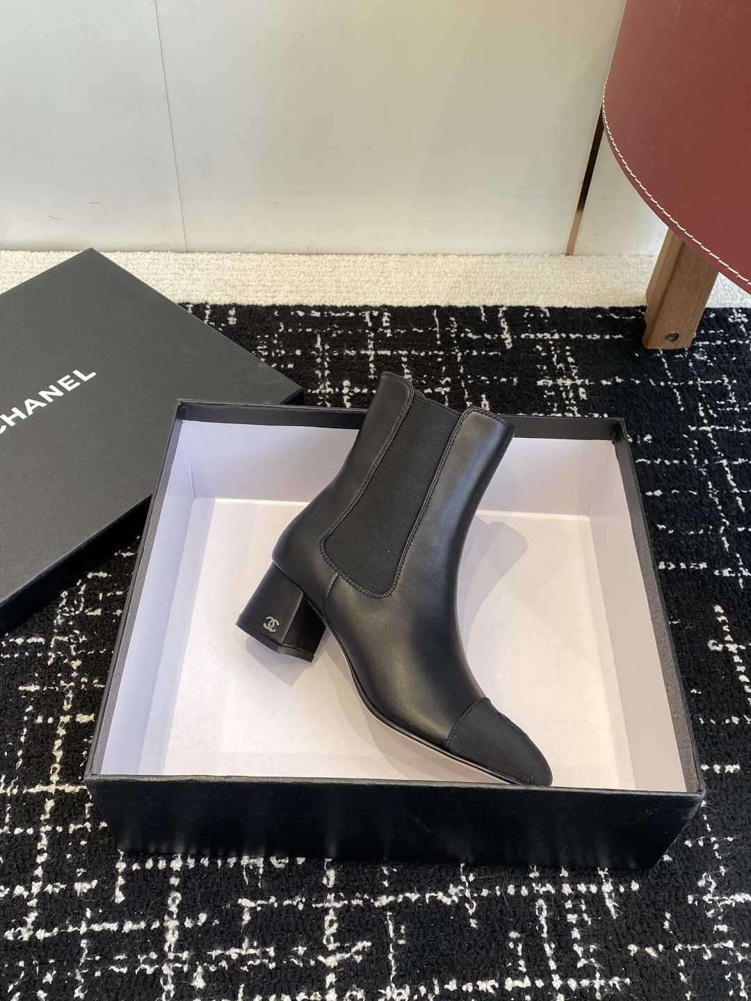 Chanel black leather Chelsea boots with signature CC logo on the toe cap and heel, displayed on a black box. - Hình 6