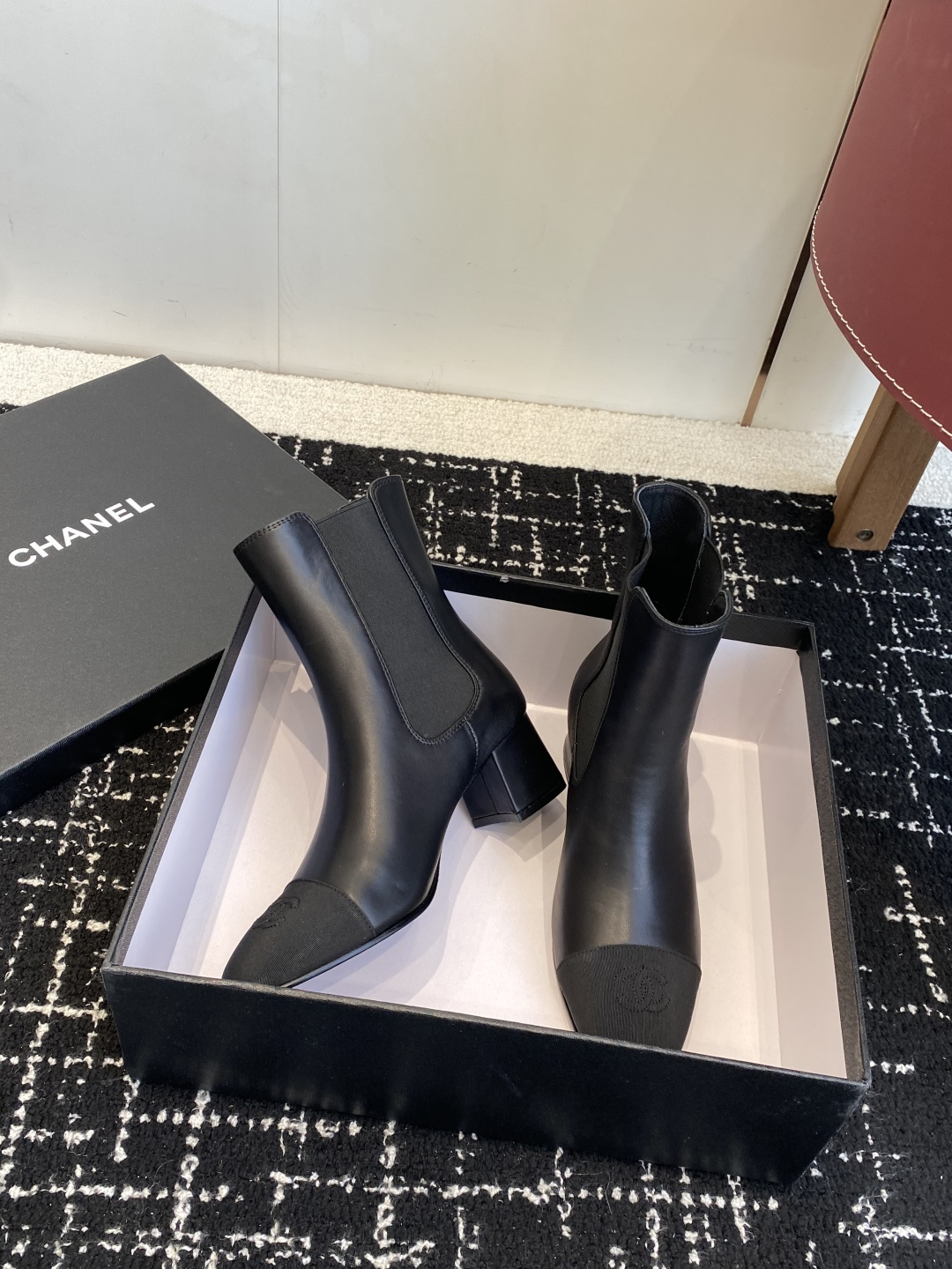 Chanel black leather Chelsea boots with signature CC logo on the toe cap and heel, displayed on a black box. - Hình 5