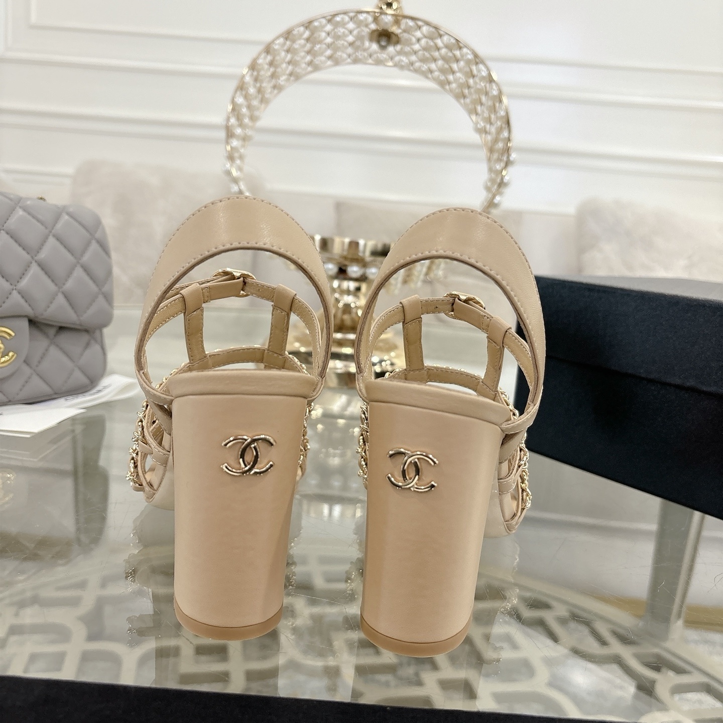 Luxury Chanel beige leather block heel sandals with black cap toes and gold-tone chain straps displayed on a glass table. - Hình 8