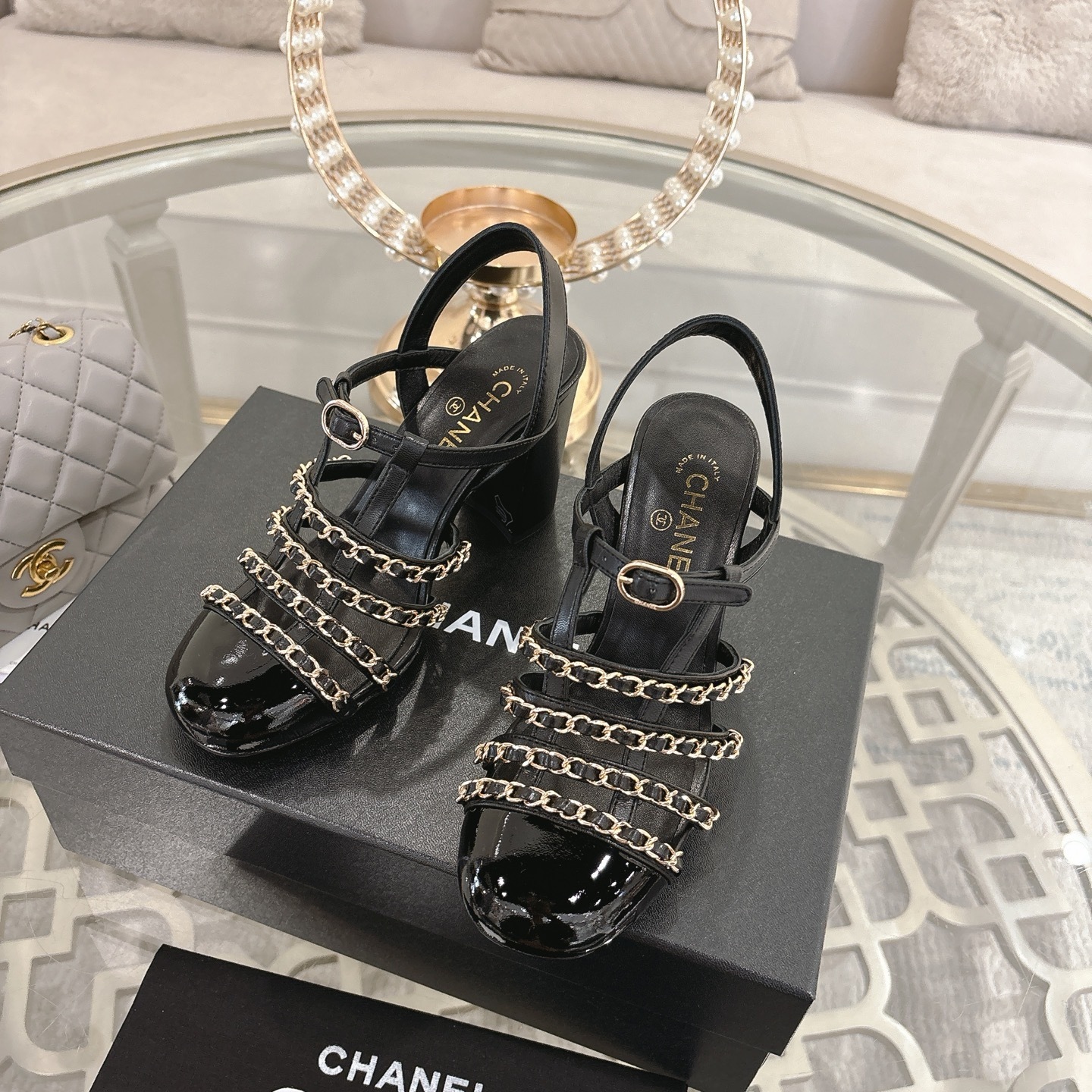 Pair of Chanel black leather sandals with gold chain straps and block heels displayed on a decorative glass table. - Hình 6