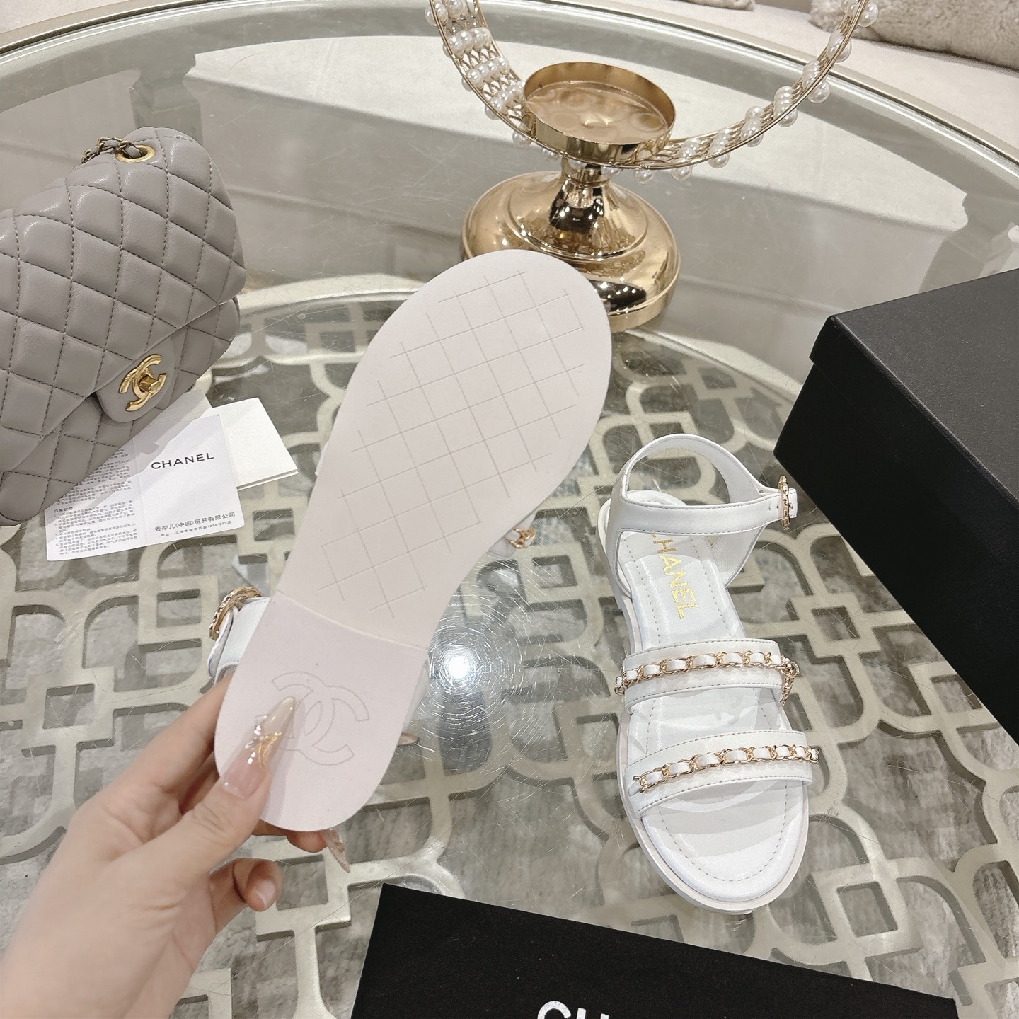 A pair of Chanel white leather flat sandals with gold chain link straps and CC logo charm displayed on a glass table. - Hình 9