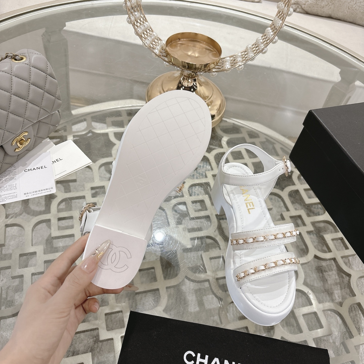 Elegant white platform sandals with gold chain-link straps and adjustable ankle buckles displayed on a glass table. - Hình 9