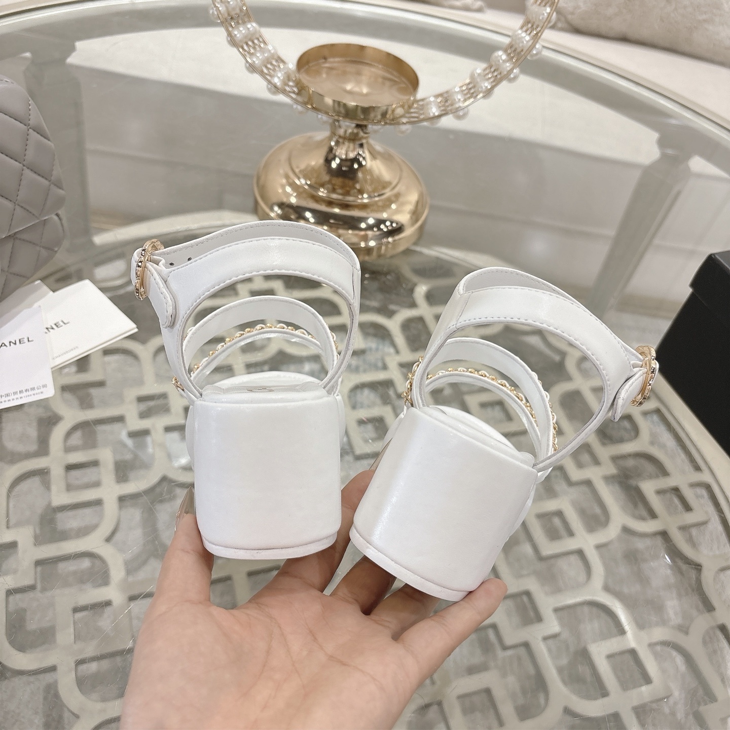 Elegant white platform sandals with gold chain-link straps and adjustable ankle buckles displayed on a glass table. - Hình 8