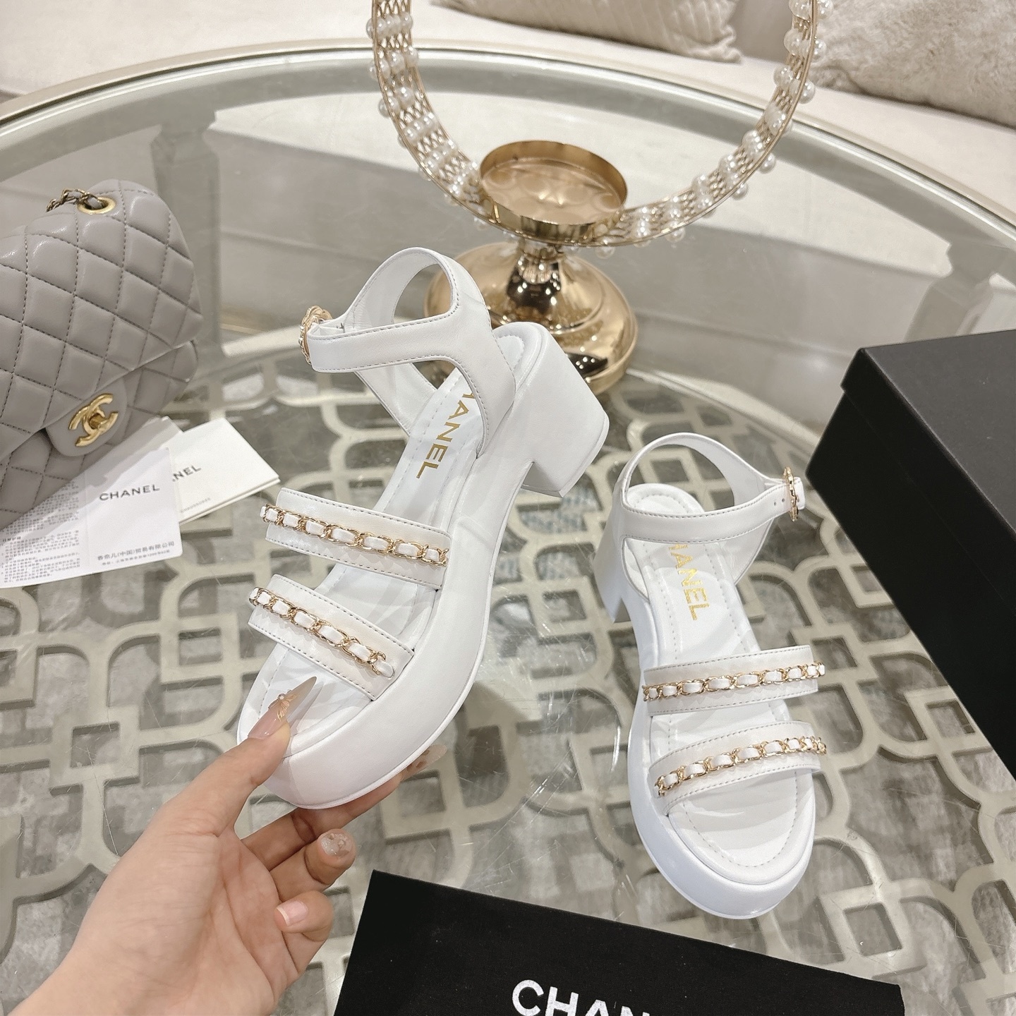 Elegant white platform sandals with gold chain-link straps and adjustable ankle buckles displayed on a glass table. - Hình 4