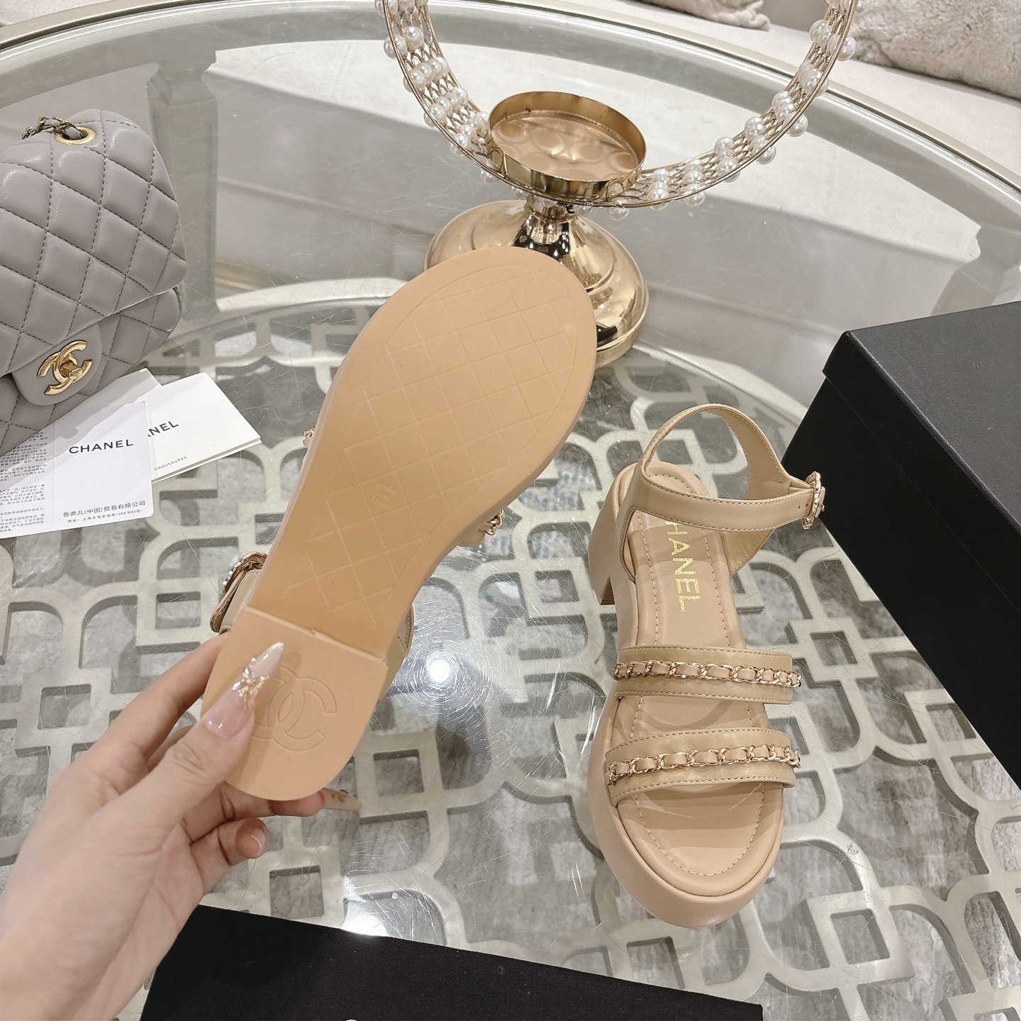 Elegant beige platform sandals with gold chain link straps and adjustable ankle buckle displayed on a glass table. - Hình 9