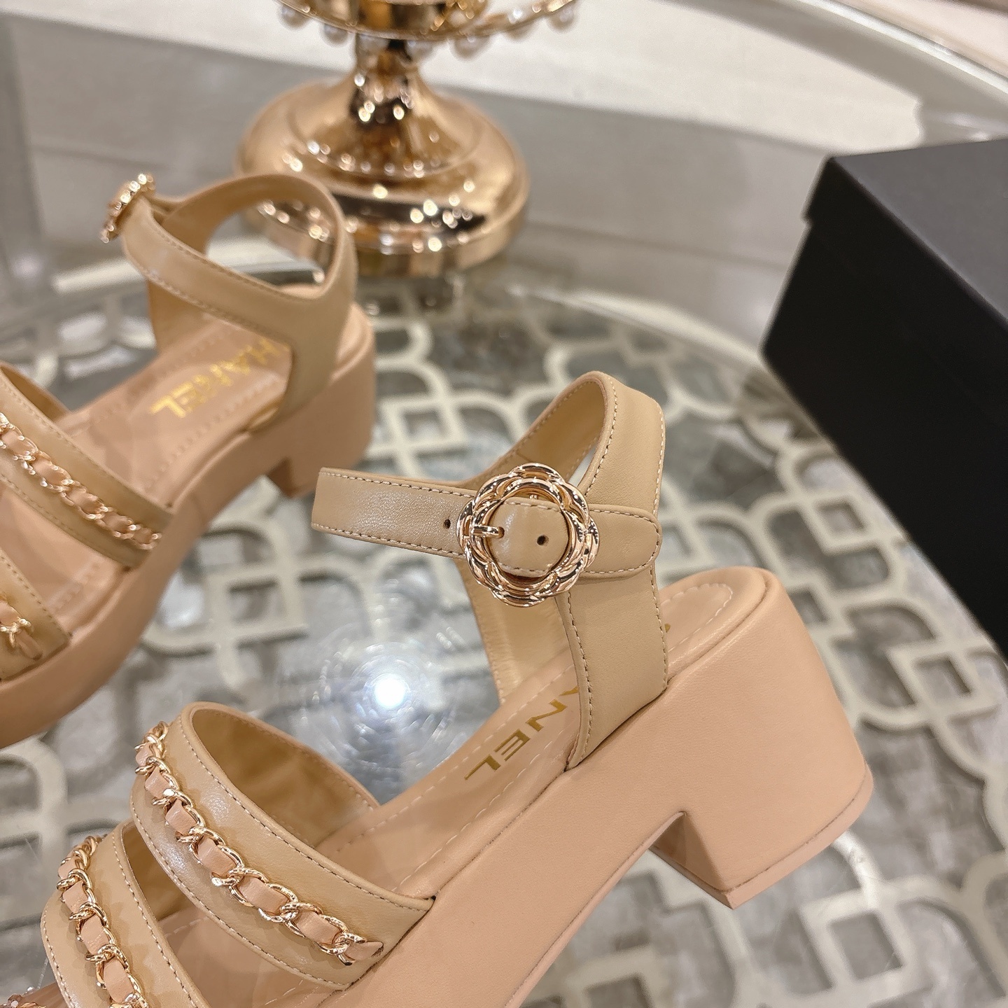 Elegant beige platform sandals with gold chain link straps and adjustable ankle buckle displayed on a glass table. - Hình 8