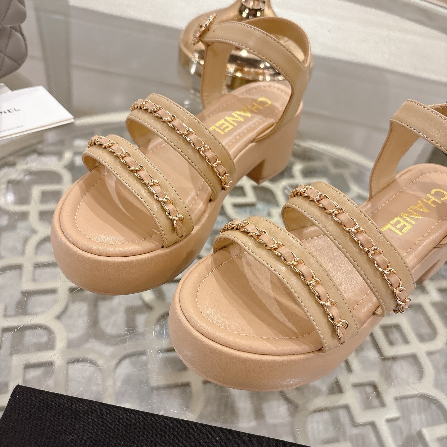Elegant beige platform sandals with gold chain link straps and adjustable ankle buckle displayed on a glass table. - Hình 7