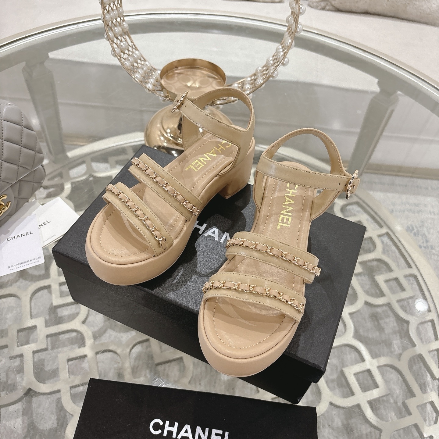 Elegant beige platform sandals with gold chain link straps and adjustable ankle buckle displayed on a glass table. - Hình 6