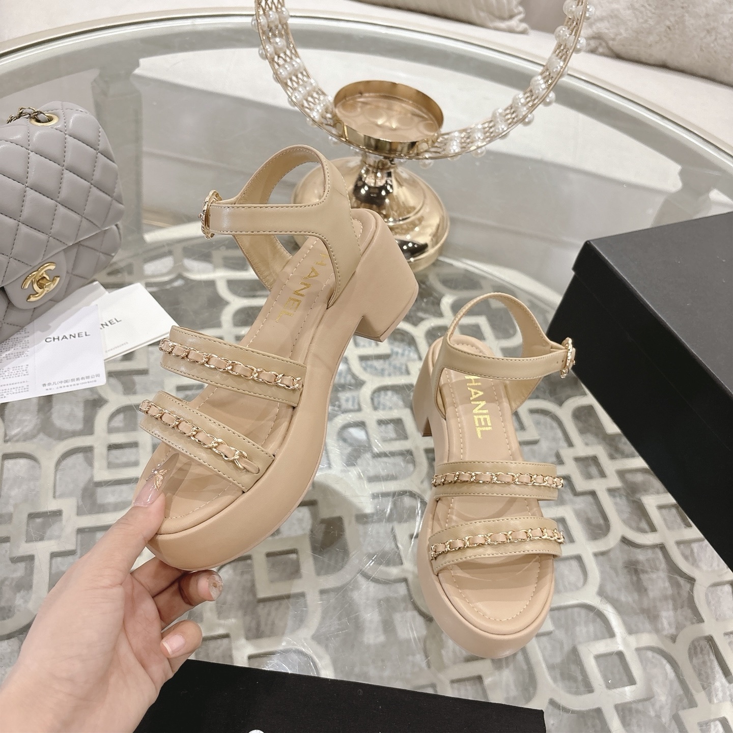Elegant beige platform sandals with gold chain link straps and adjustable ankle buckle displayed on a glass table. - Hình 4