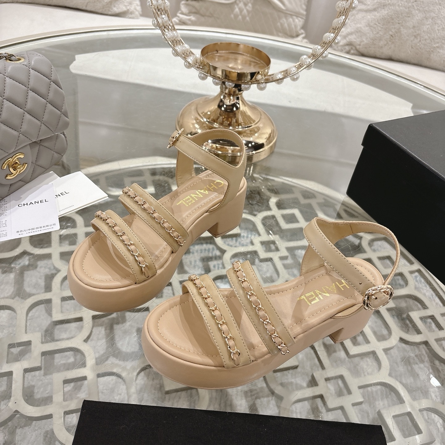 Elegant beige platform sandals with gold chain link straps and adjustable ankle buckle displayed on a glass table. - Hình 3