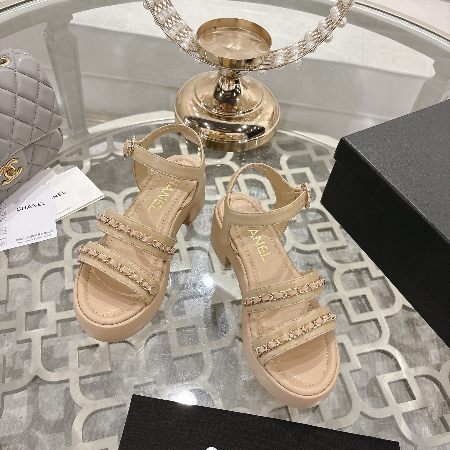 Elegant beige platform sandals with gold chain link straps and adjustable ankle buckle displayed on a glass table. - Hình 2