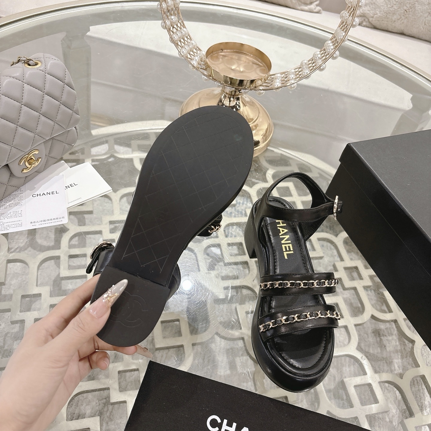Elegant black platform sandals with two gold chain straps and an ankle buckle displayed on a decorative glass table. - Hình 9