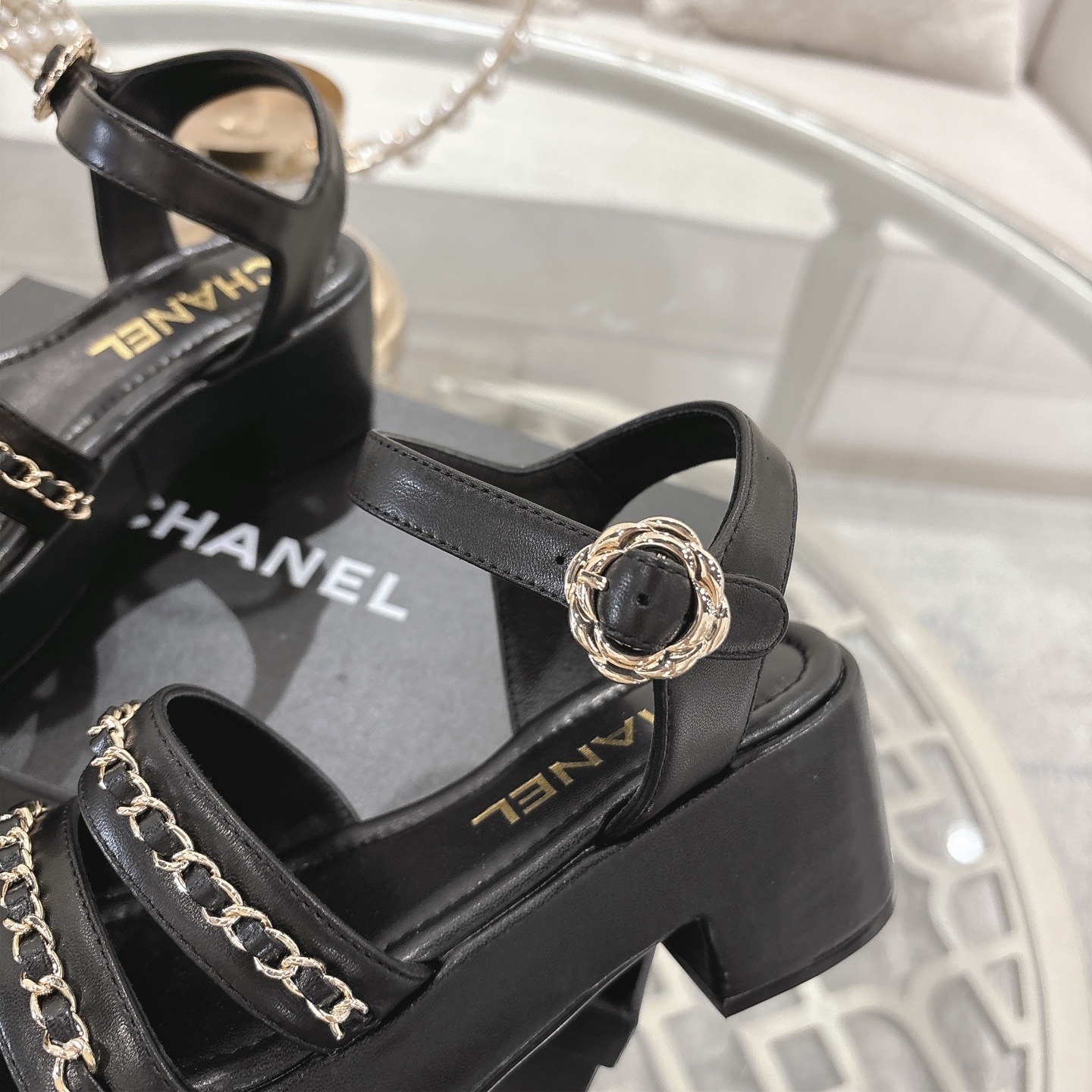 Elegant black platform sandals with two gold chain straps and an ankle buckle displayed on a decorative glass table. - Hình 8