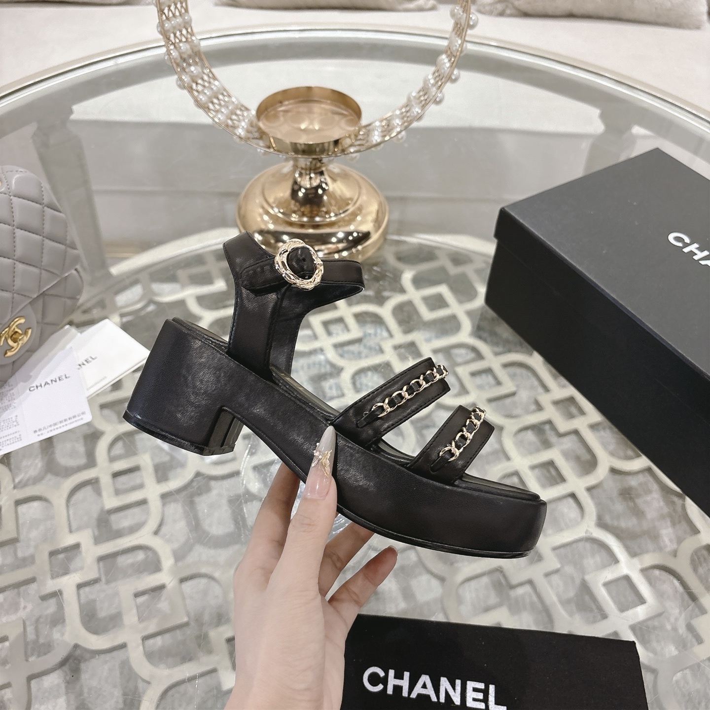 Elegant black platform sandals with two gold chain straps and an ankle buckle displayed on a decorative glass table. - Hình 5