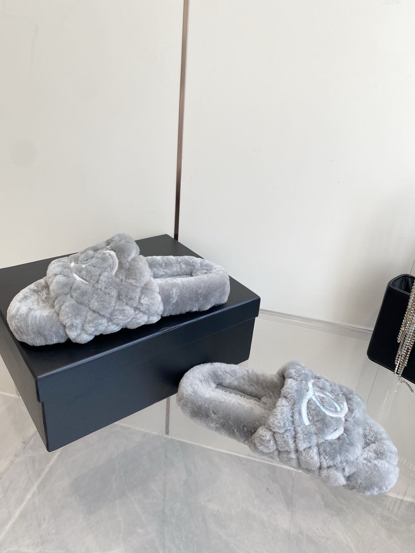 A pair of premium grey quilted faux fur slides featuring an interlocking logo design on a marble surface. - Hình 7