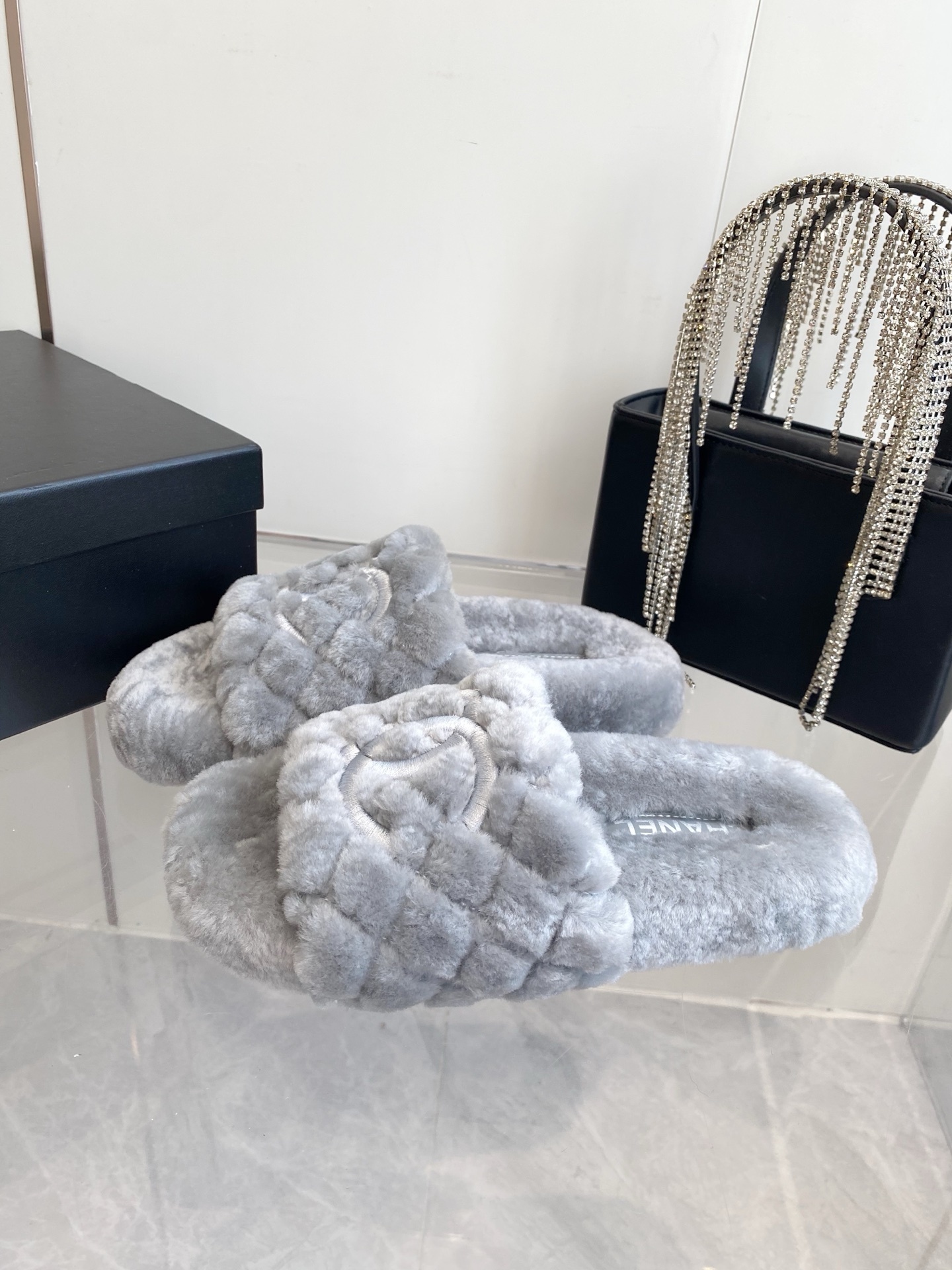 A pair of premium grey quilted faux fur slides featuring an interlocking logo design on a marble surface. - Hình 2
