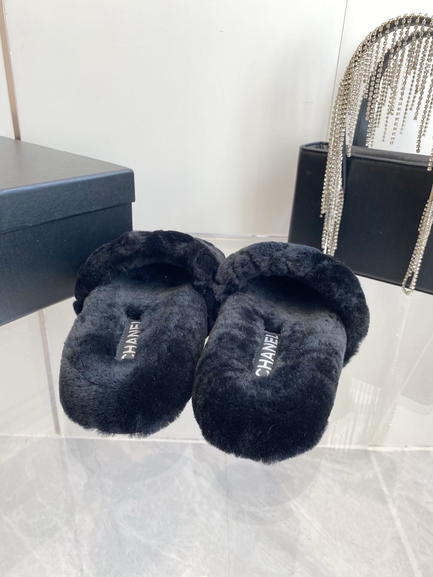 Pair of black plush faux fur slippers with embroidered interlocking C logo on a marble surface near a black handbag. - Hình 8