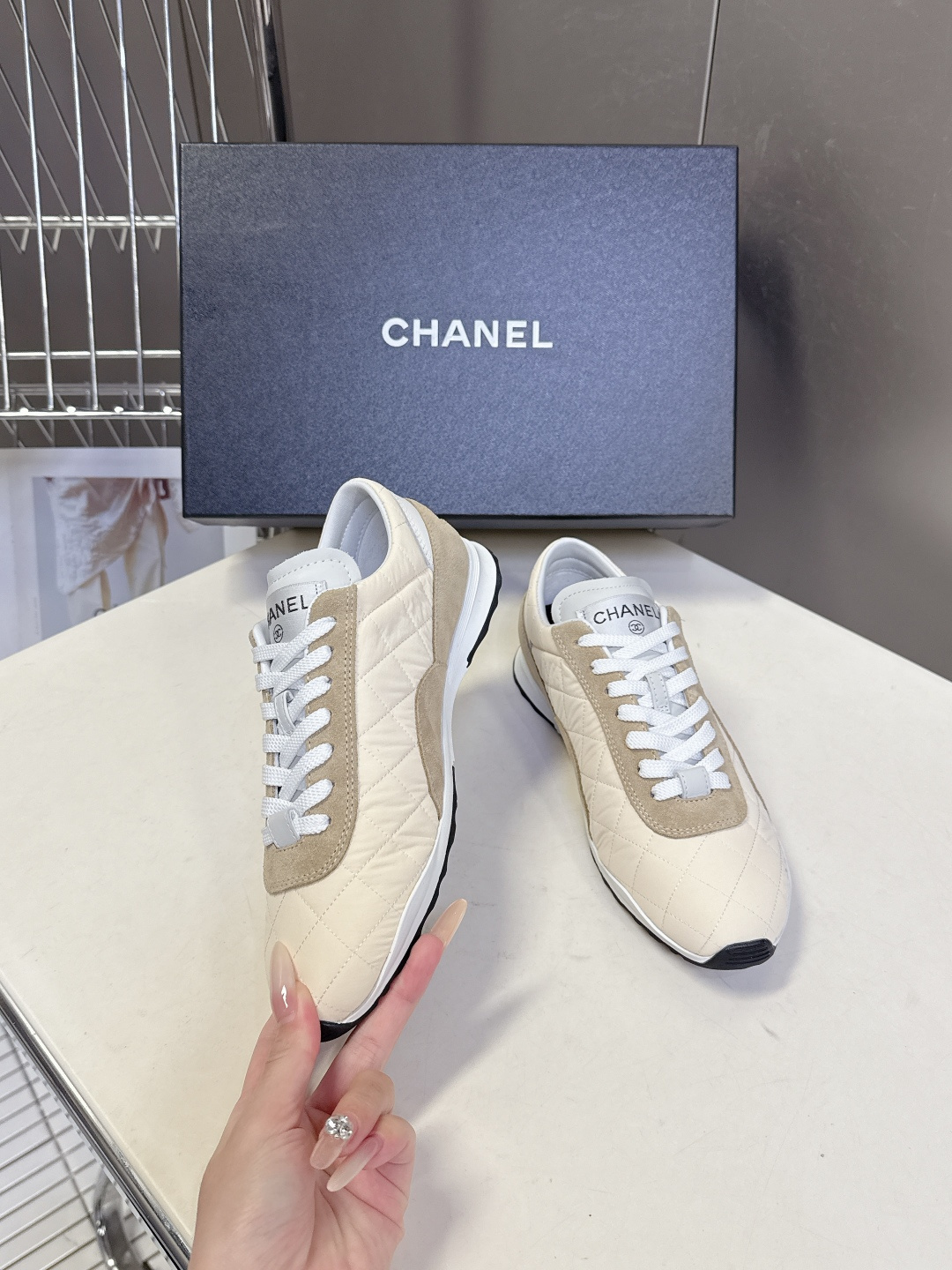 A pair of luxury Chanel quilted sneakers in beige and tan suede featuring the CC logo, placed next to a blue Chanel box. - Hình 4