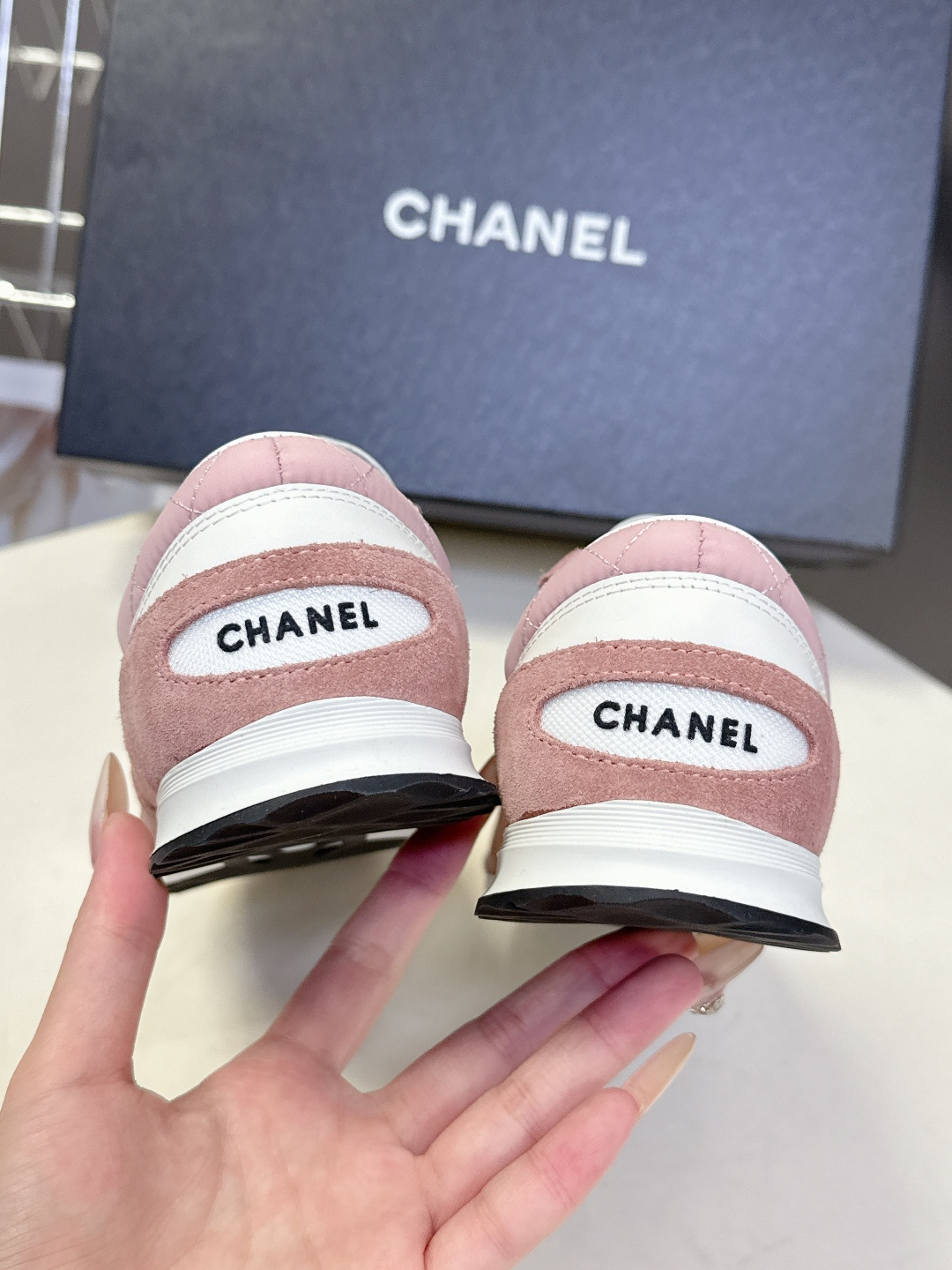 A pair of luxury pink quilted Chanel sneakers with white laces displayed next to their original black Chanel box. - Hình 9