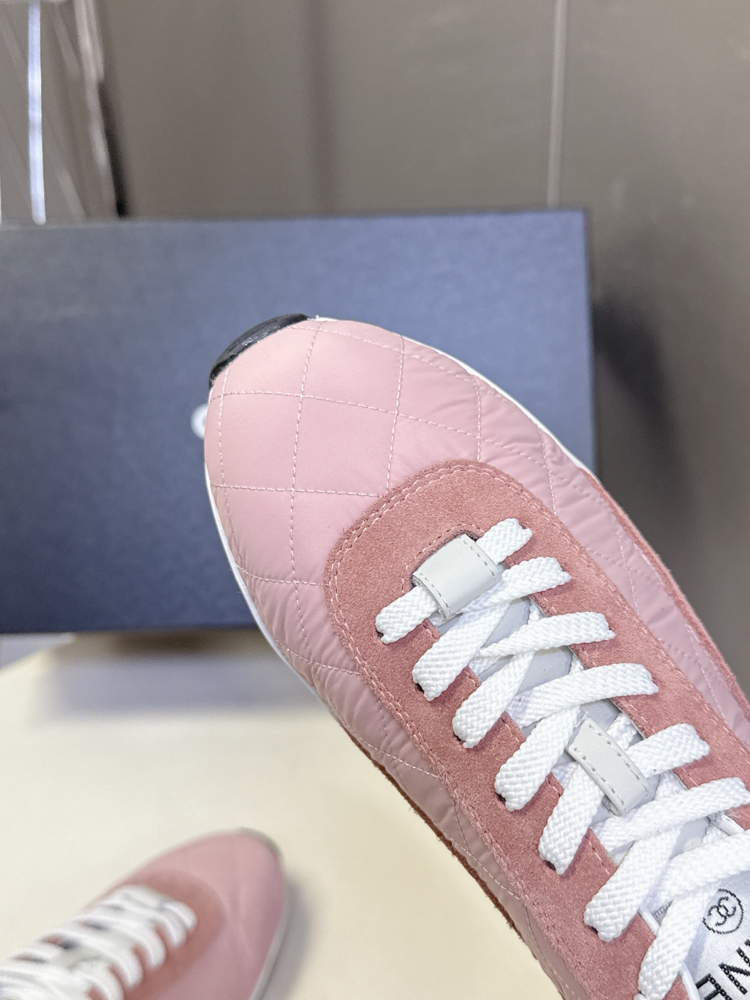 A pair of luxury pink quilted Chanel sneakers with white laces displayed next to their original black Chanel box. - Hình 8