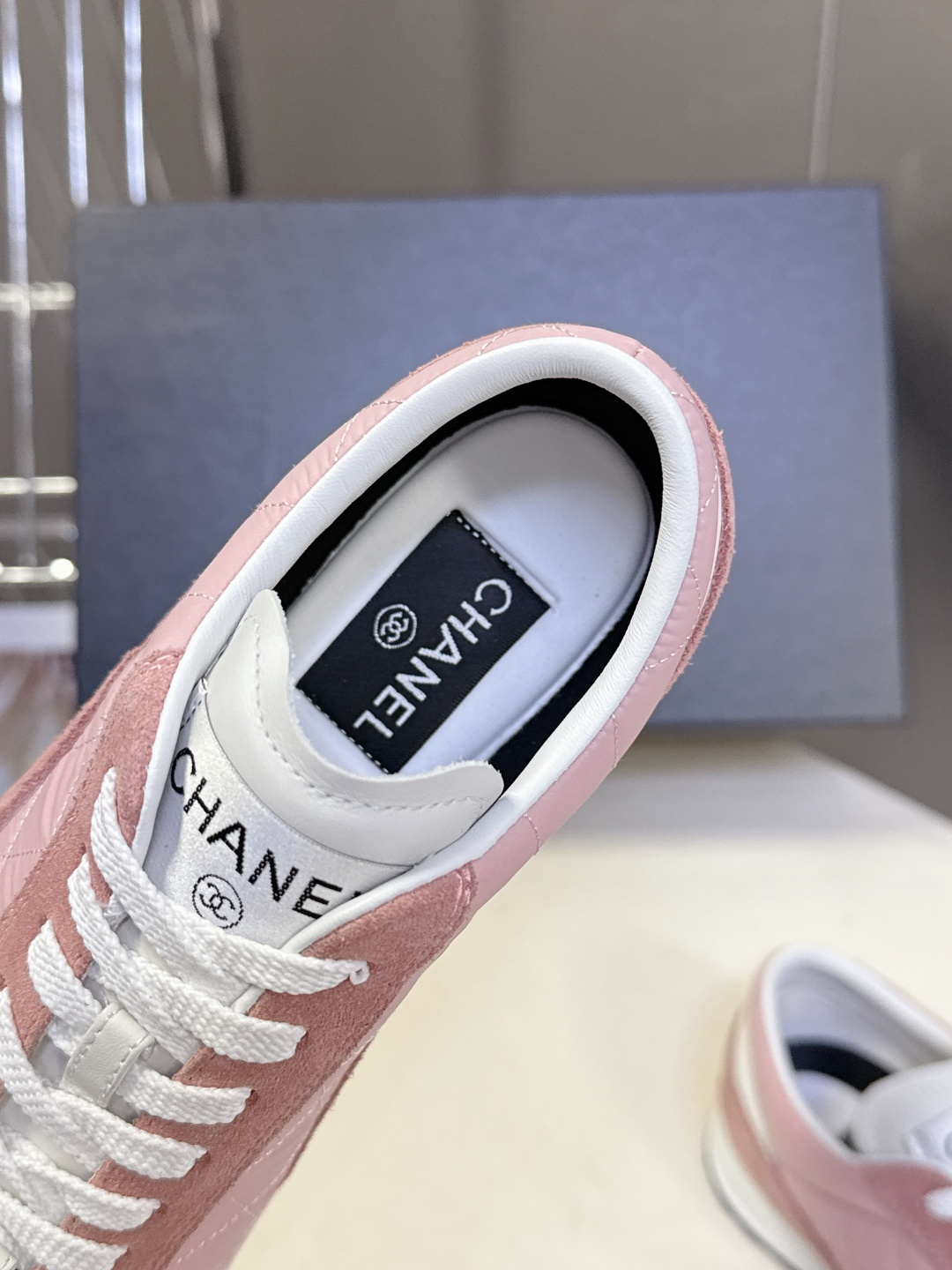 A pair of luxury pink quilted Chanel sneakers with white laces displayed next to their original black Chanel box. - Hình 7
