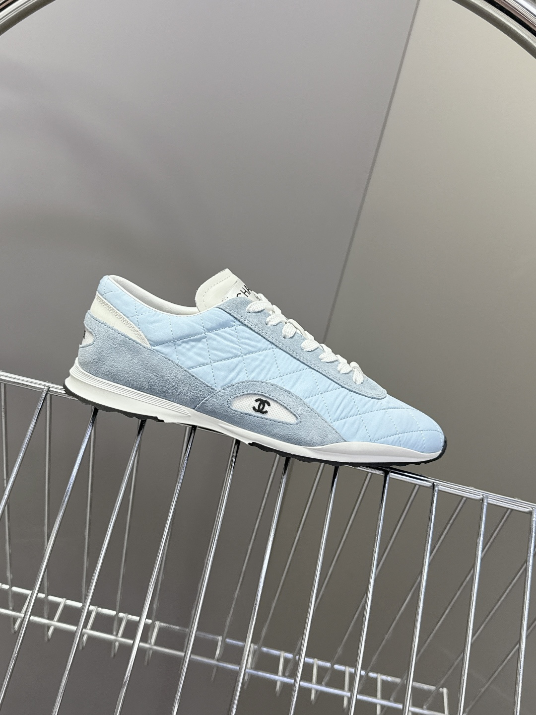 A pair of light blue Chanel quilted sneakers with white laces and suede accents next to a black Chanel shoe box. - Hình 5