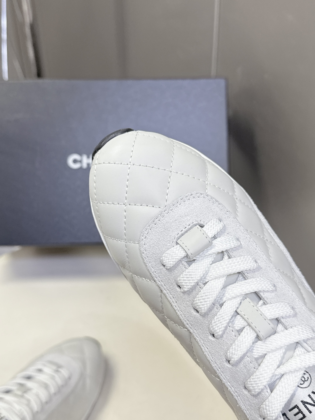 A pair of luxury white Chanel quilted leather sneakers with suede accents next to an original Chanel box. - Hình 8