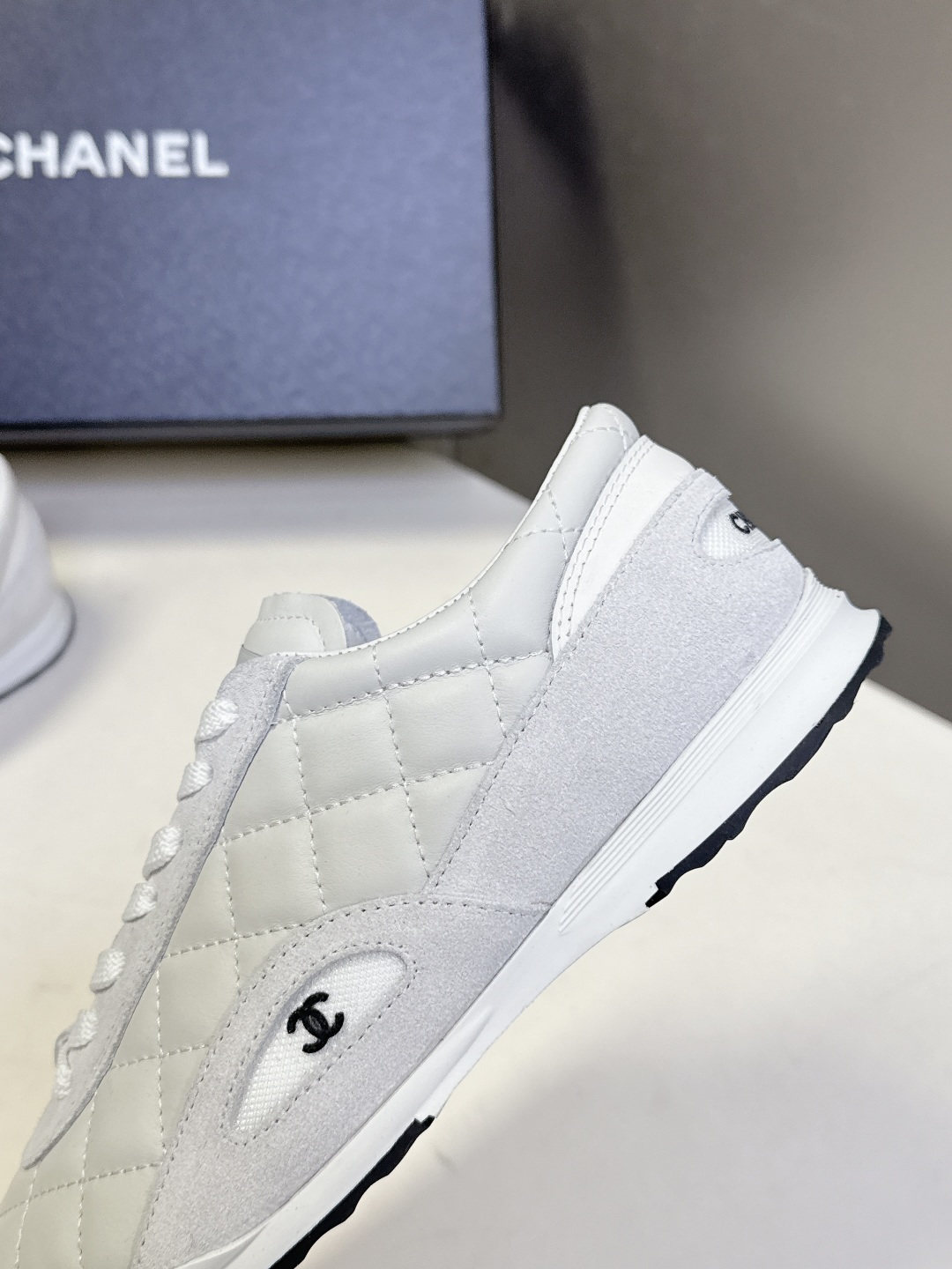 A pair of luxury white Chanel quilted leather sneakers with suede accents next to an original Chanel box. - Hình 7