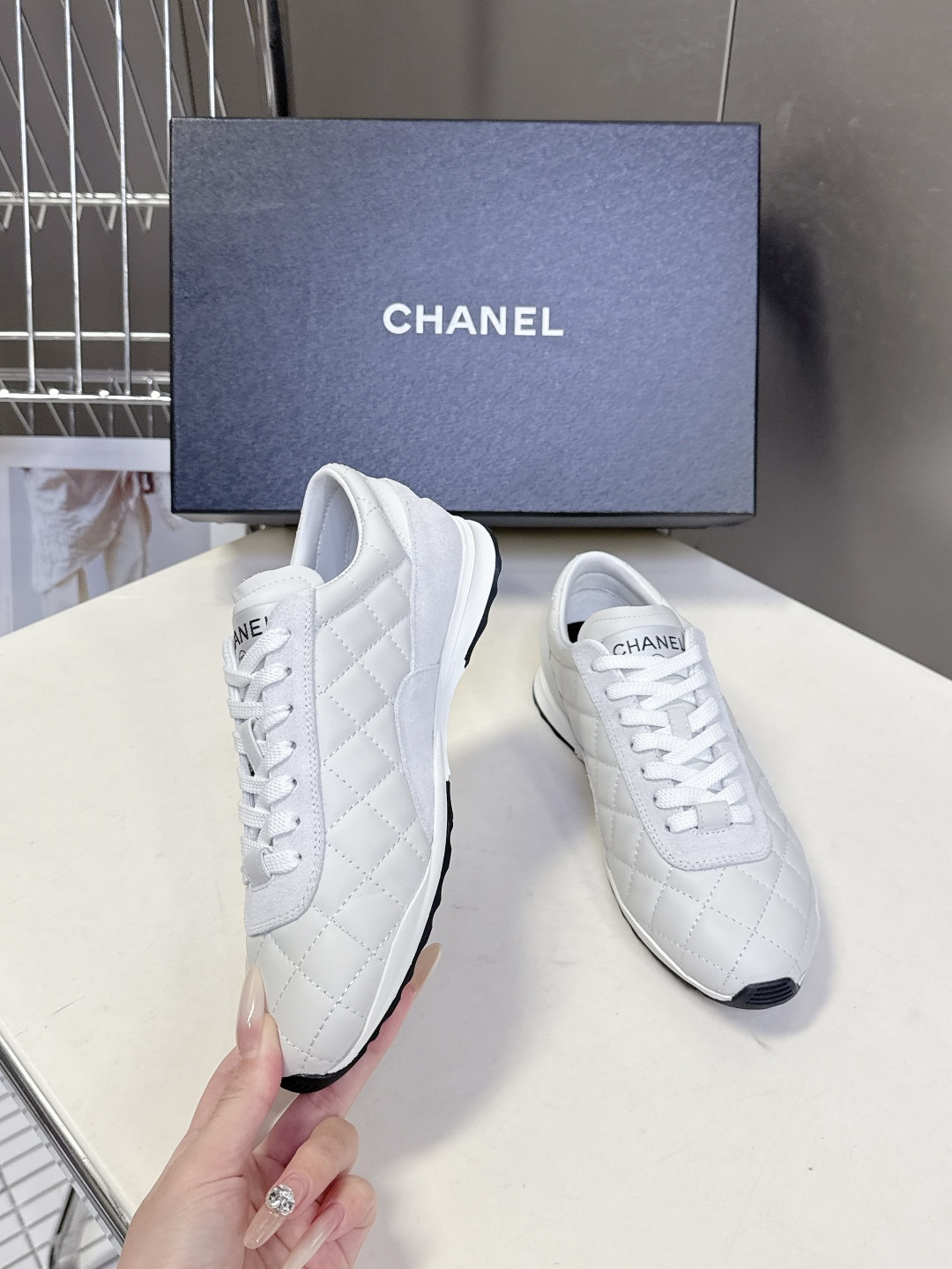 A pair of luxury white Chanel quilted leather sneakers with suede accents next to an original Chanel box. - Hình 4