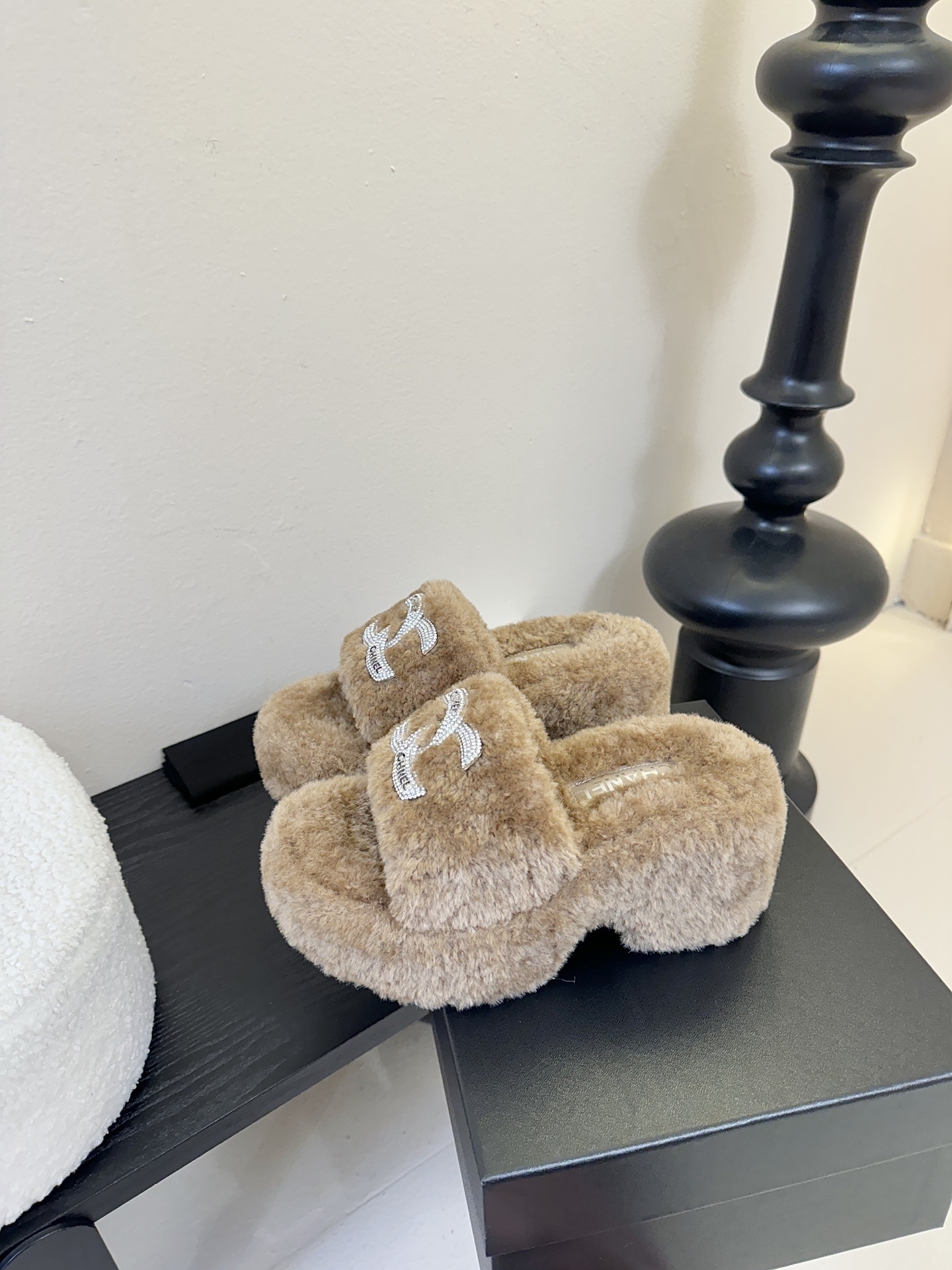 Pair of brown Chanel fluffy shearling platform slides with crystal CC logo on a black display table - Hình 5