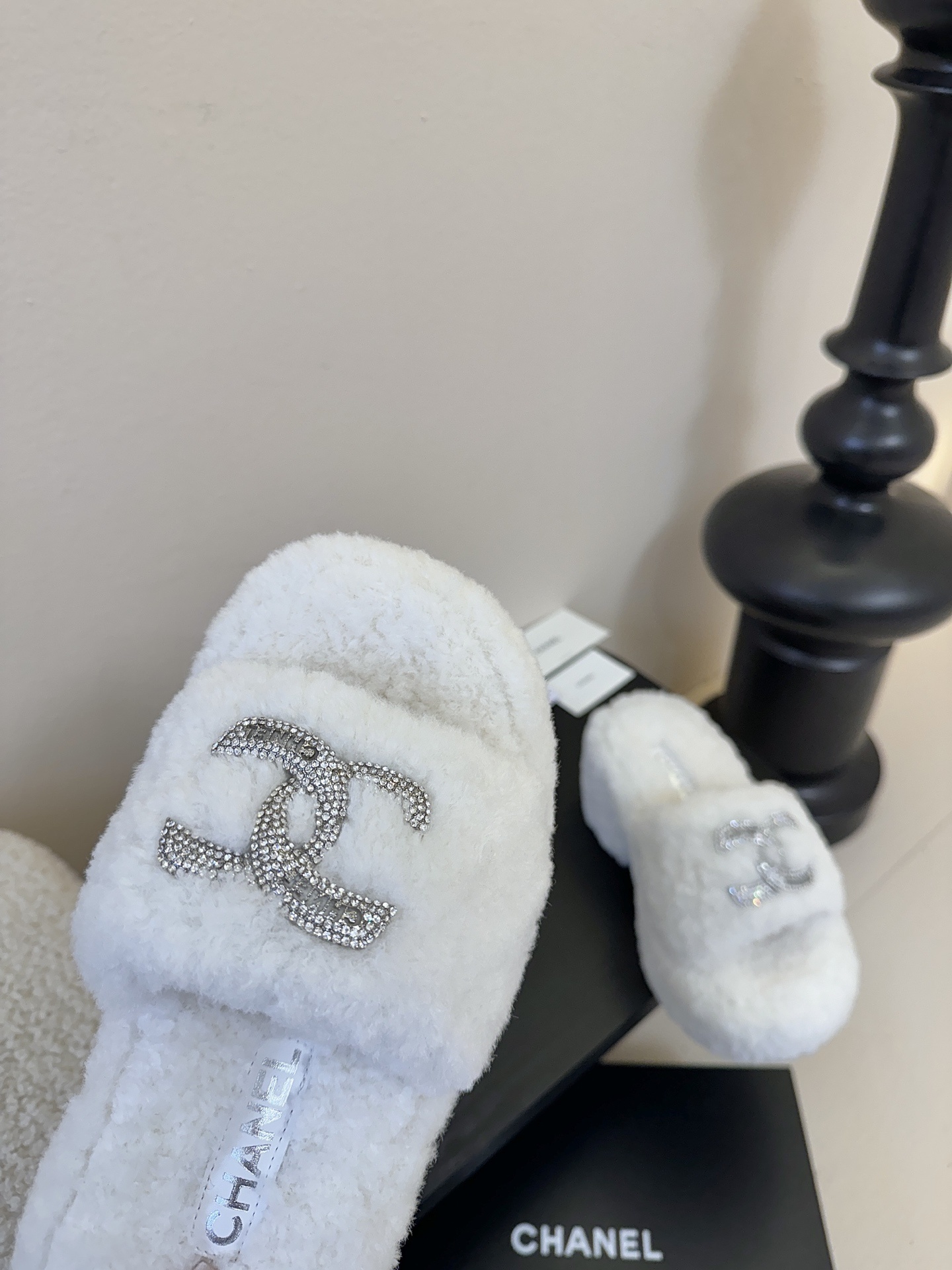 Pair of white fluffy Chanel platform slide sandals with rhinestone CC logo displayed on a black surface - Hình 6