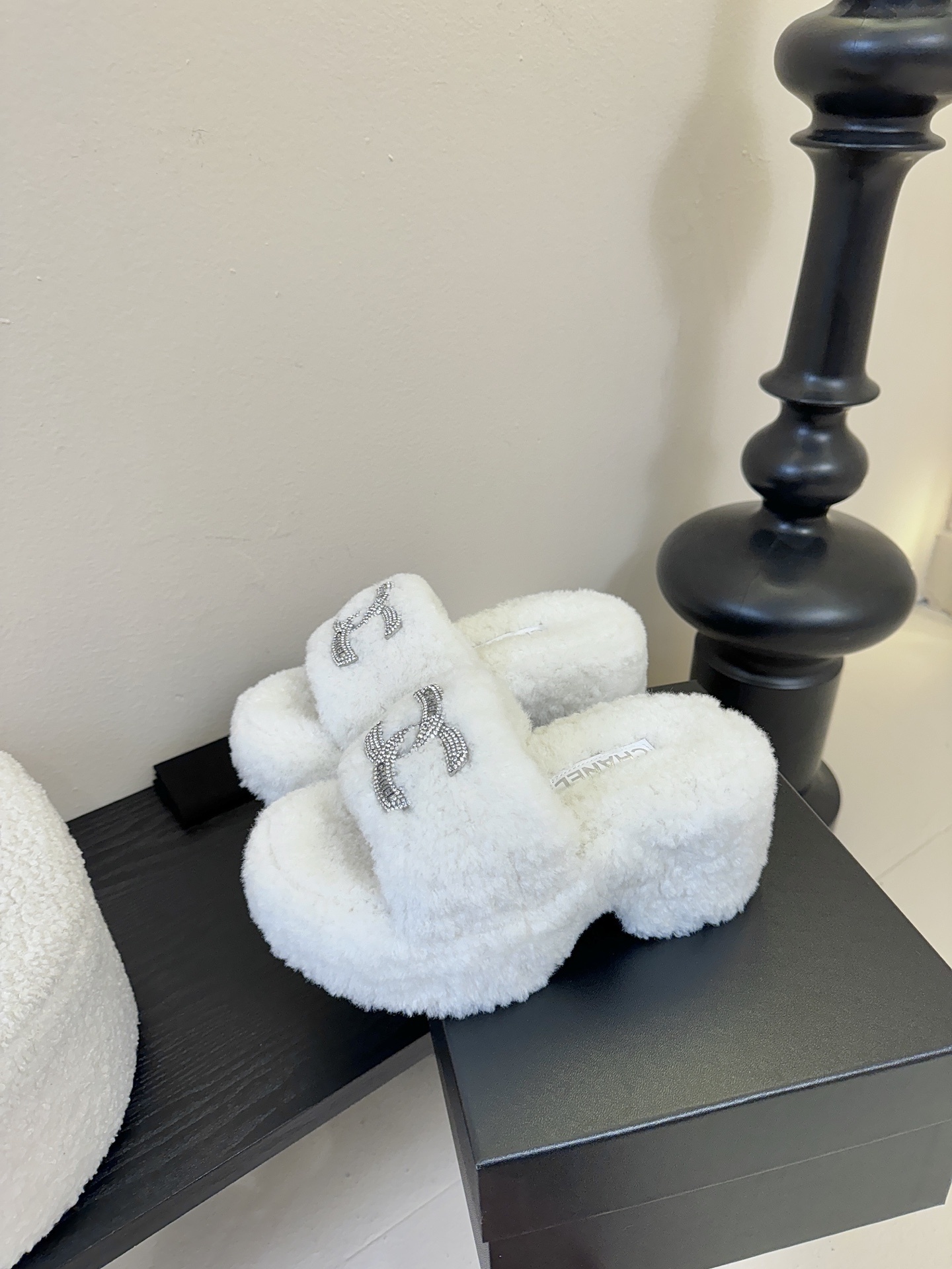Pair of white fluffy Chanel platform slide sandals with rhinestone CC logo displayed on a black surface - Hình 5