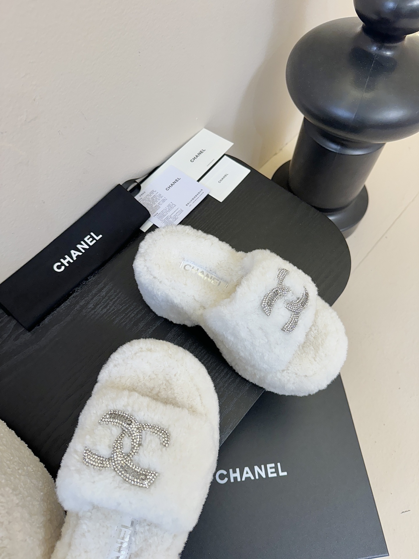 Pair of white fluffy Chanel platform slide sandals with rhinestone CC logo displayed on a black surface - Hình 4