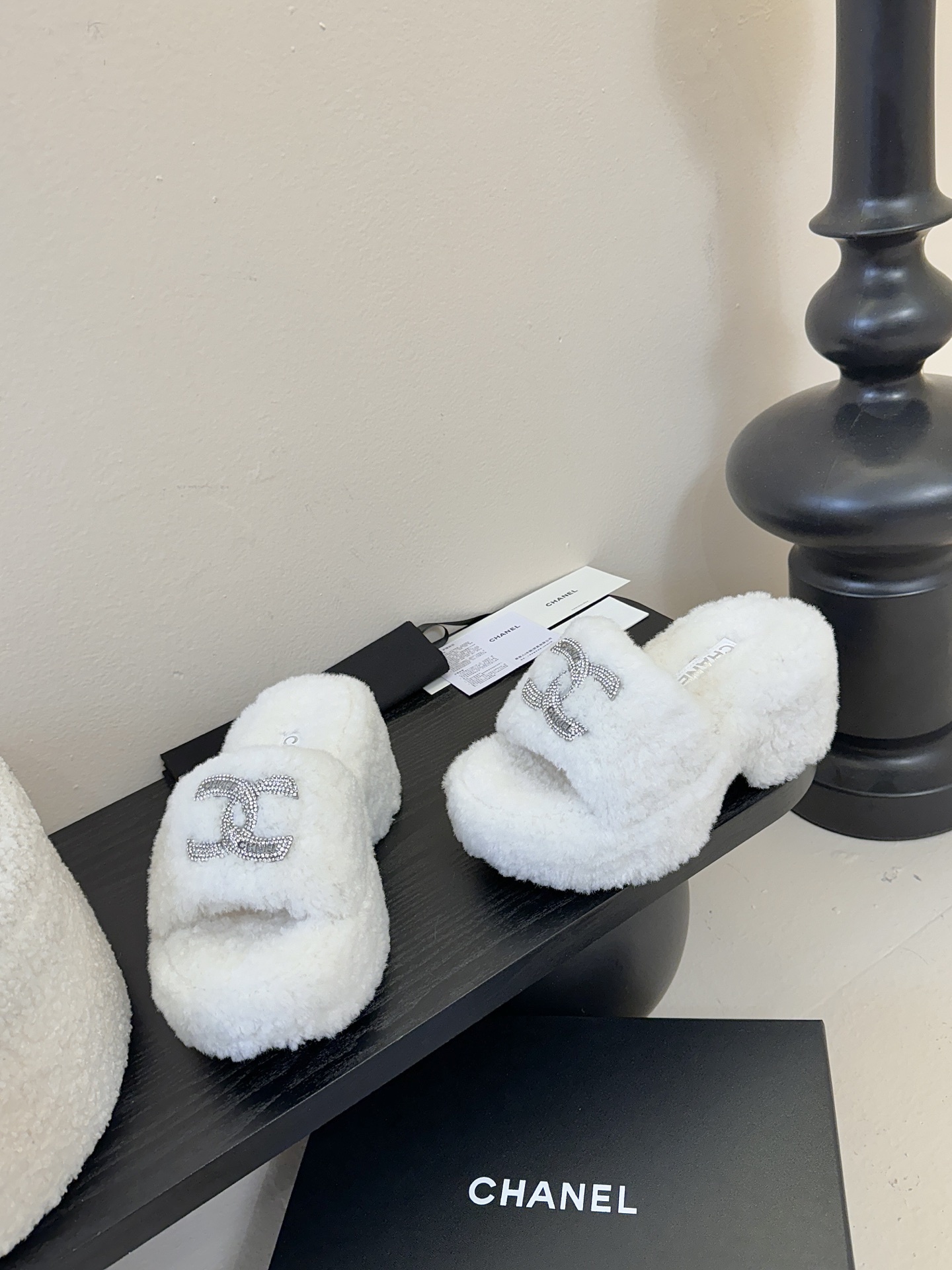 Pair of white fluffy Chanel platform slide sandals with rhinestone CC logo displayed on a black surface - Hình 3